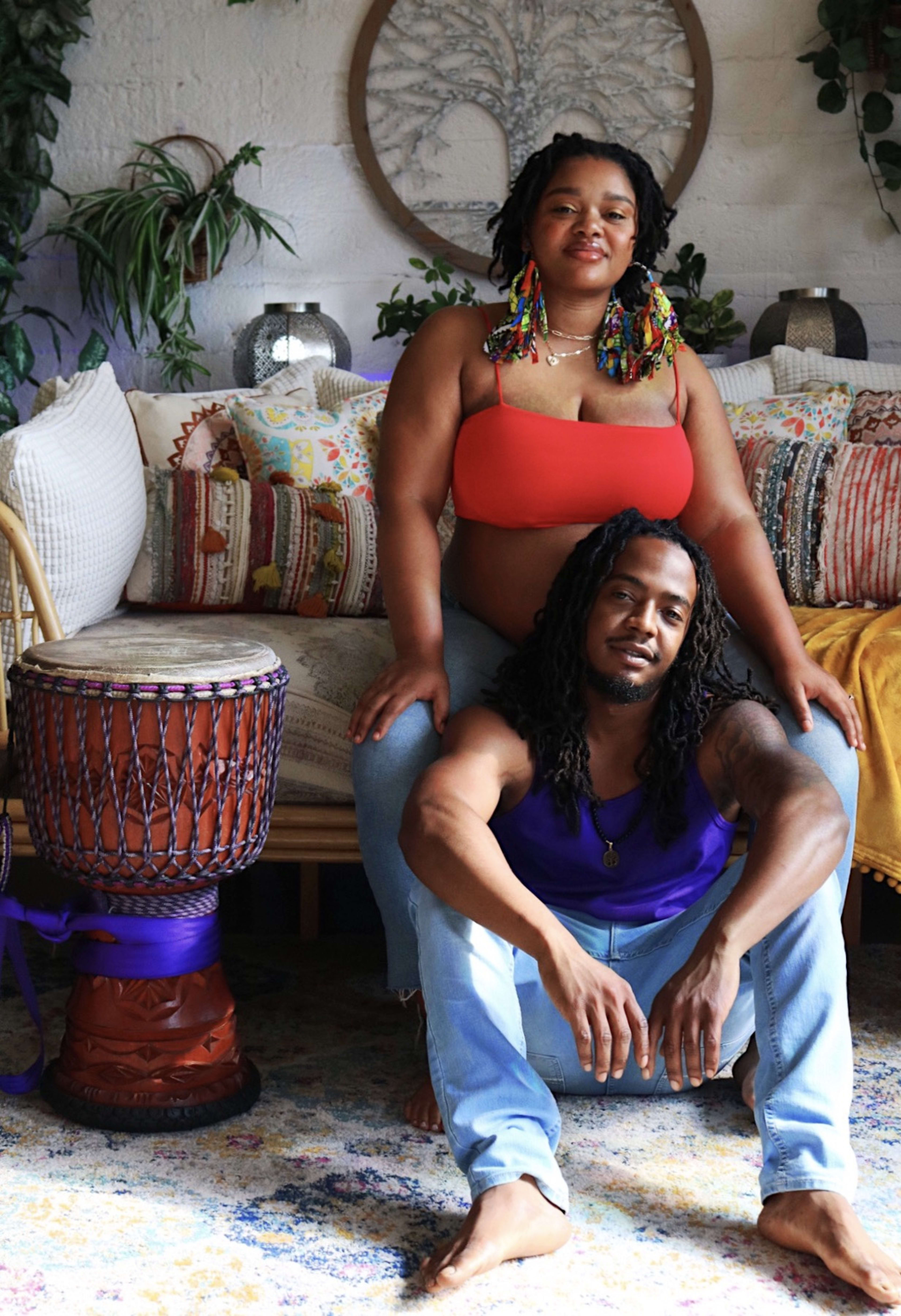 A pregnant couple sitting on a boho couch.