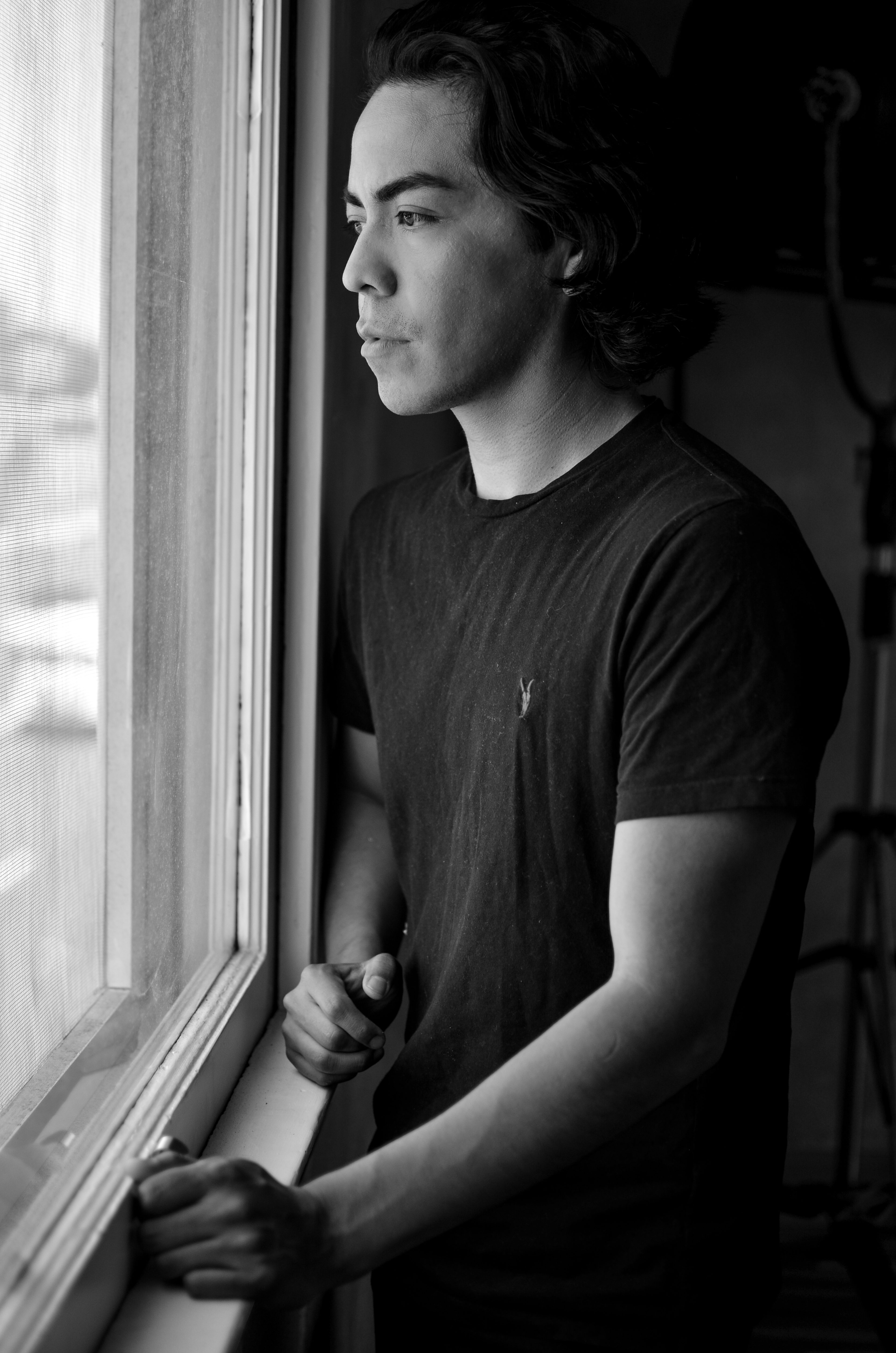 A young man posing for a black and white photo shoot looks out of a window.