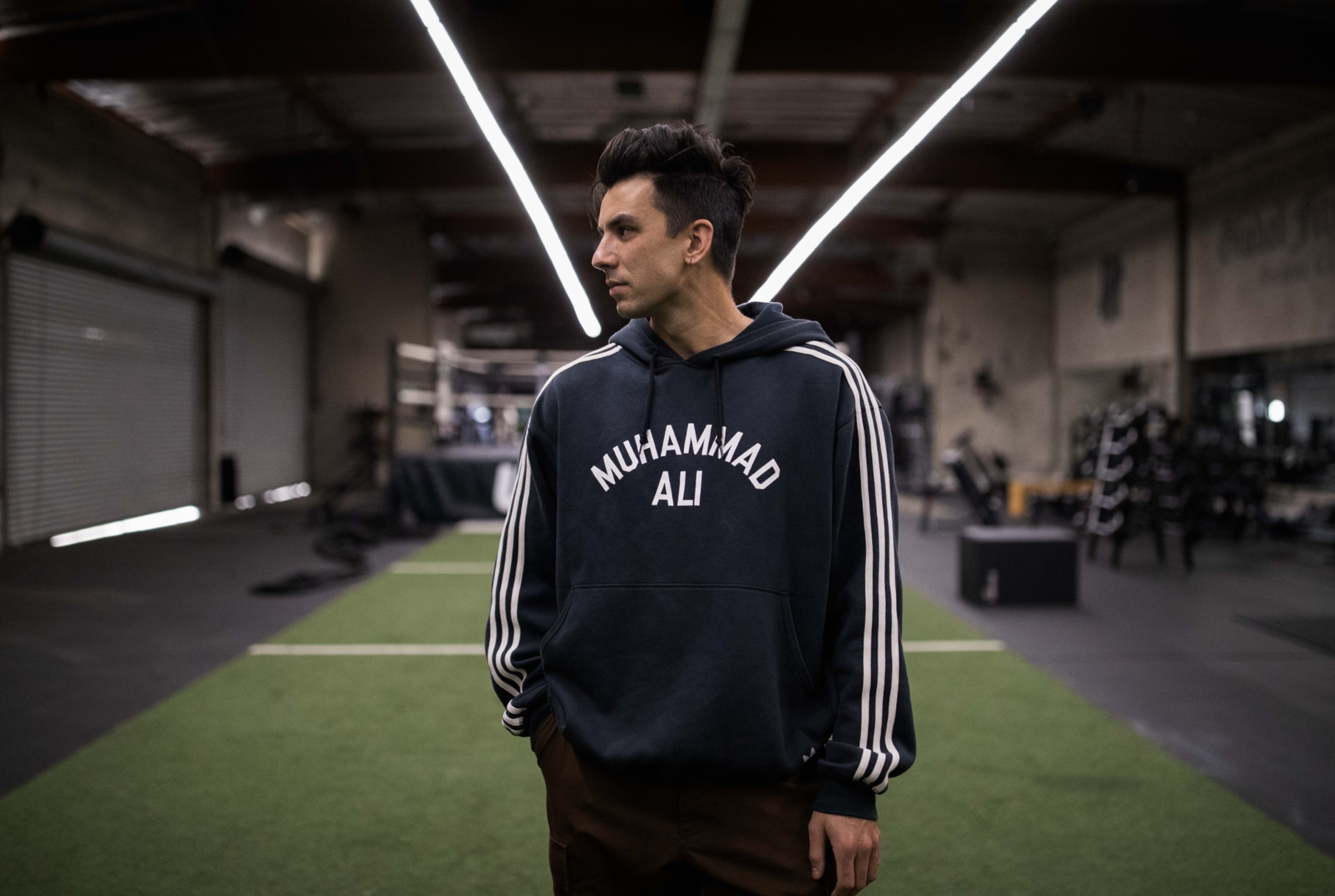 A man wearing a hoodie poses for a fitness photoshoot in the gym.