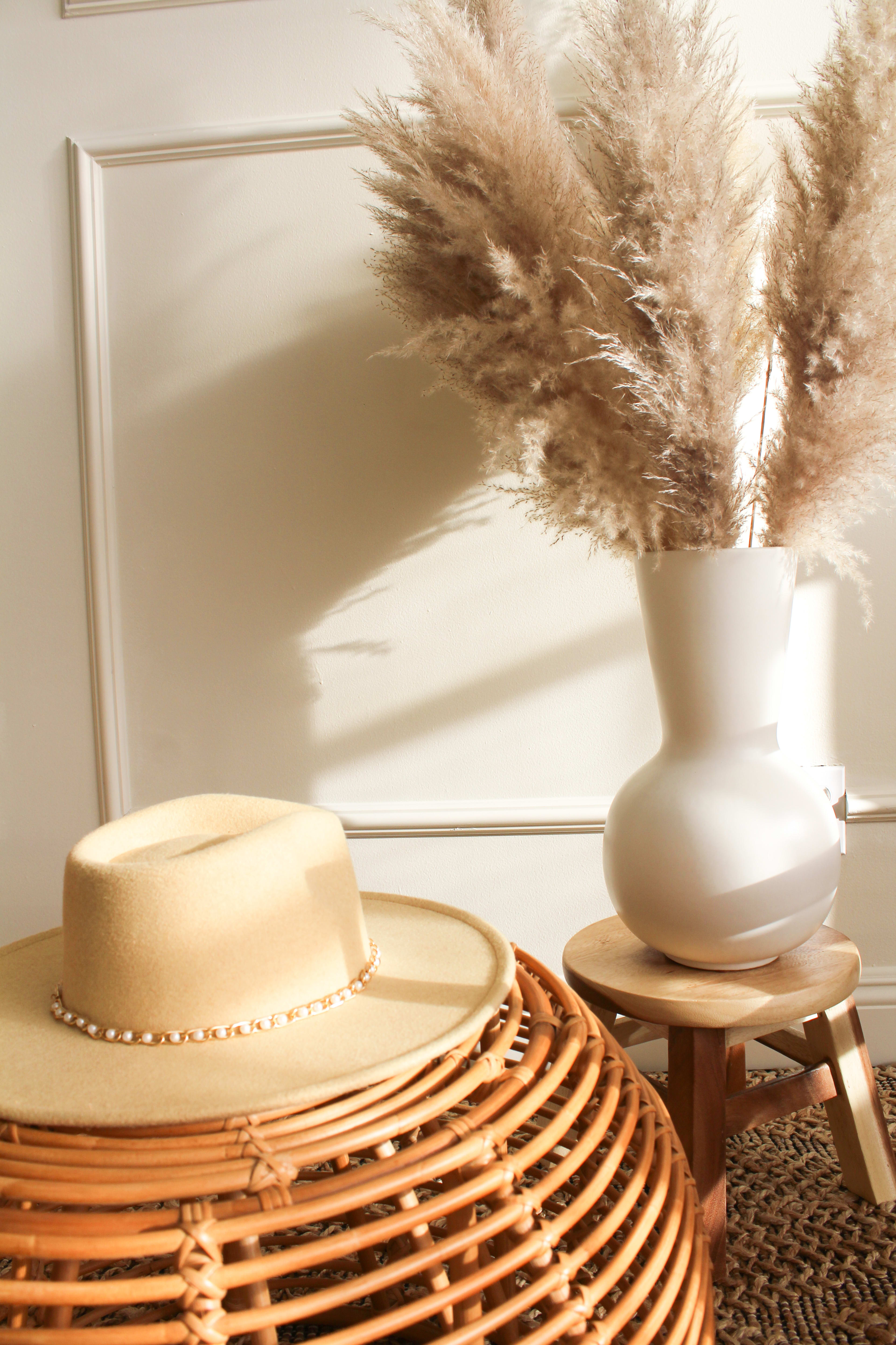 A boho photo shoot with a hat and vase on a beige table.