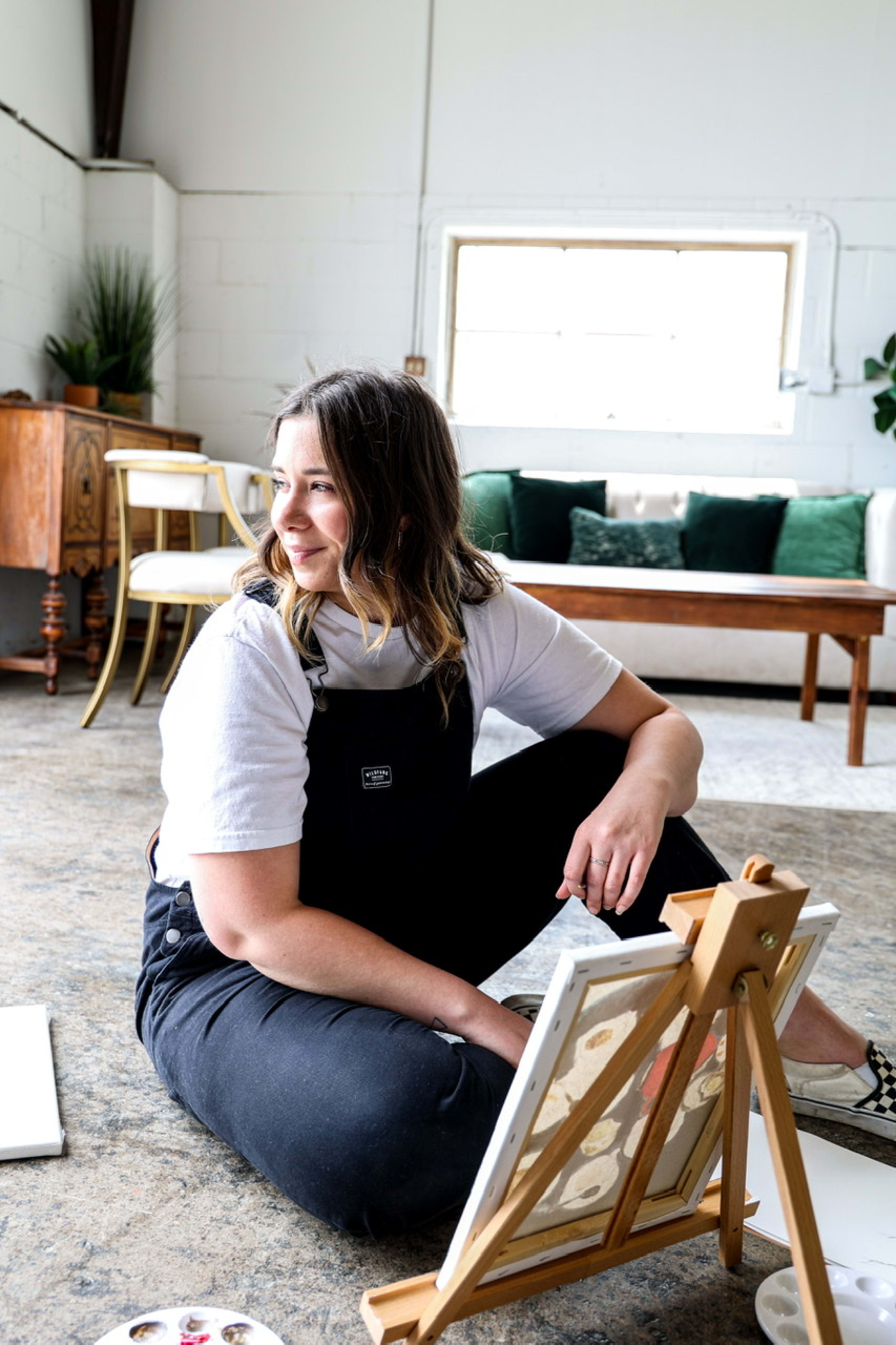 A woman sitting on the floor next to an easel during an art exhibition.