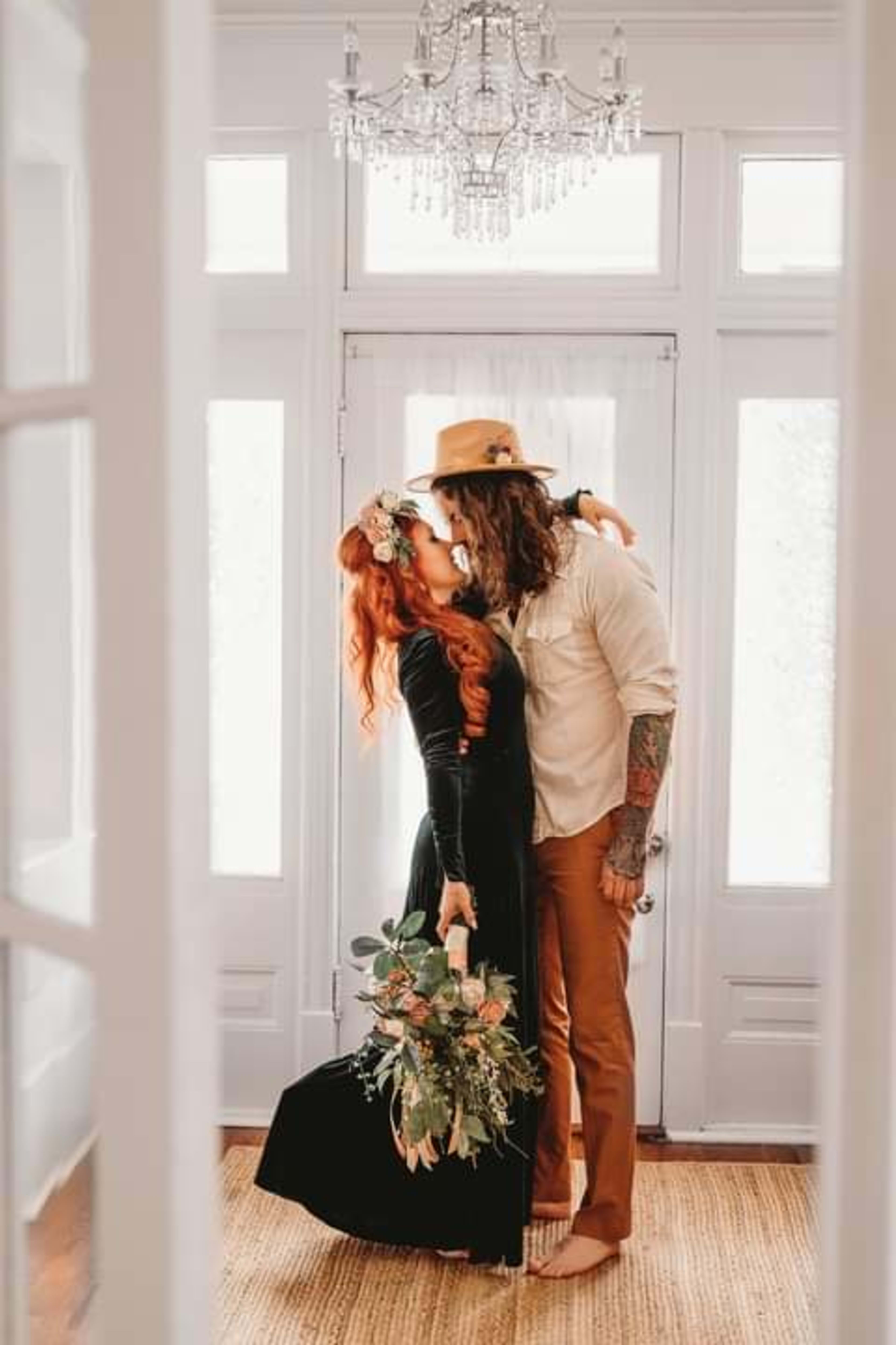 Una pareja de pie, uno junto al otro, en un decorado interior blanco.