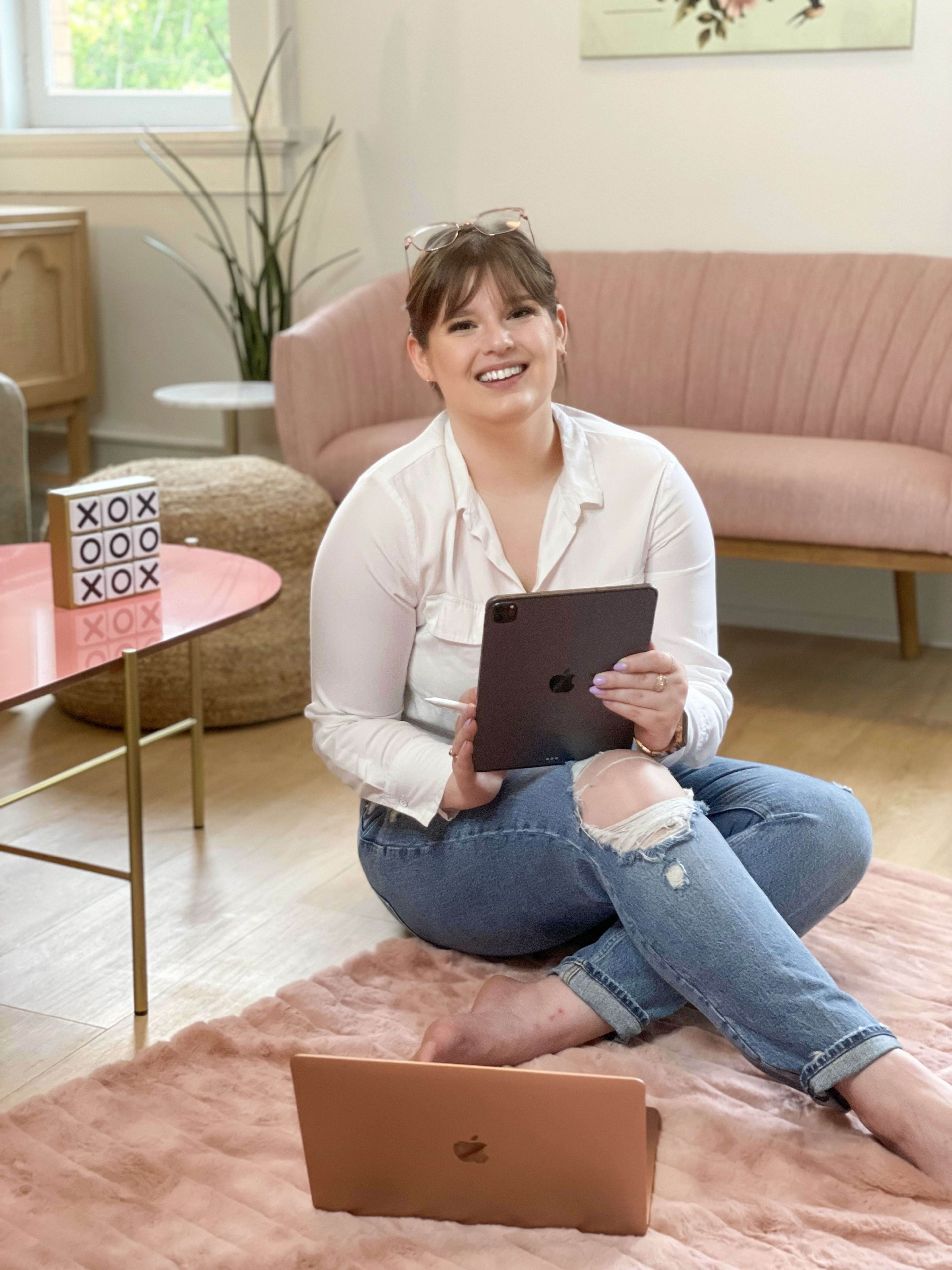 A woman sitting on the floor with a laptop amidst pink furniture and a white wall.