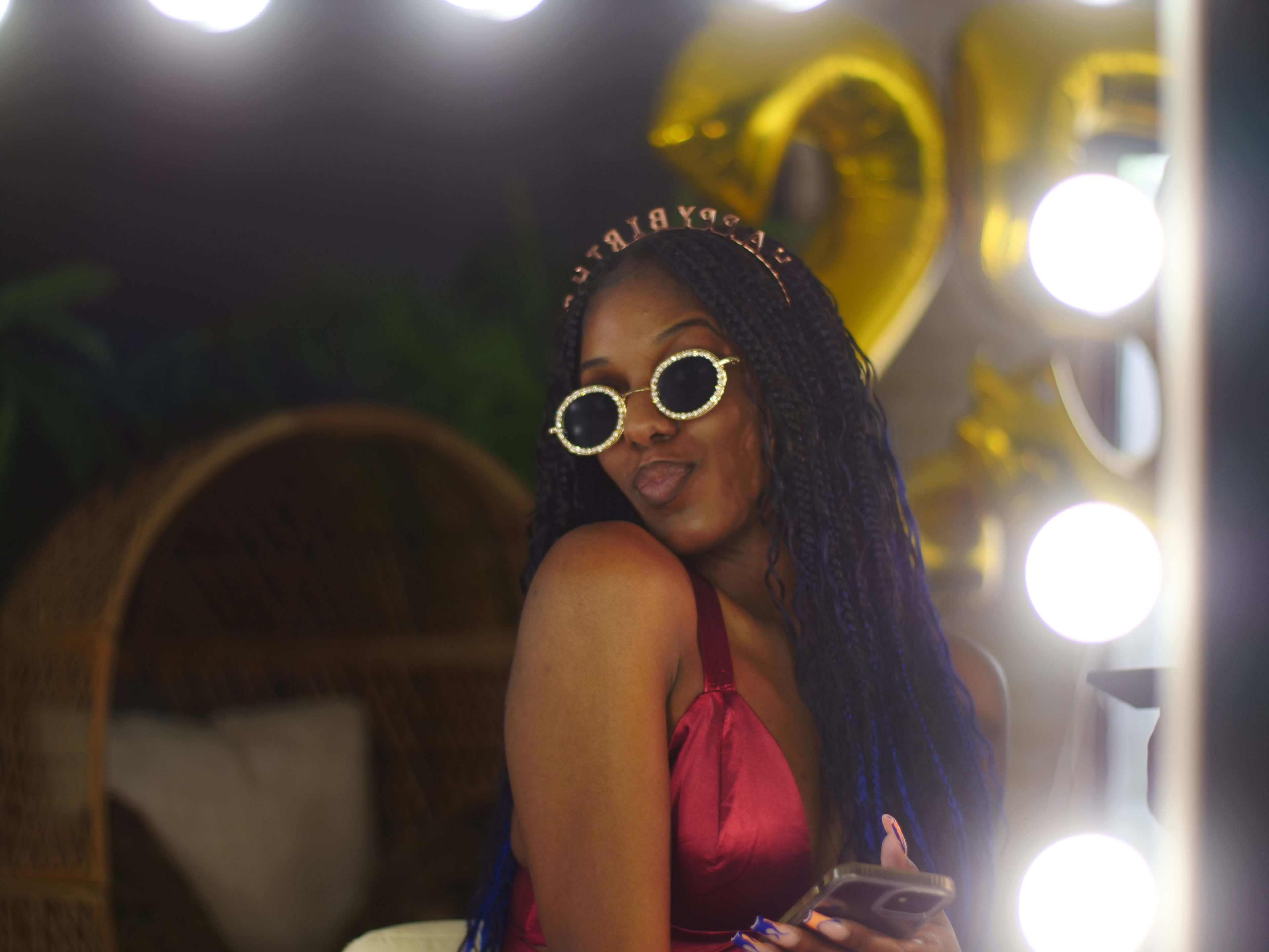 A woman in a red dress and sunglasses having a birthday photo shoot holding a mobile phone.