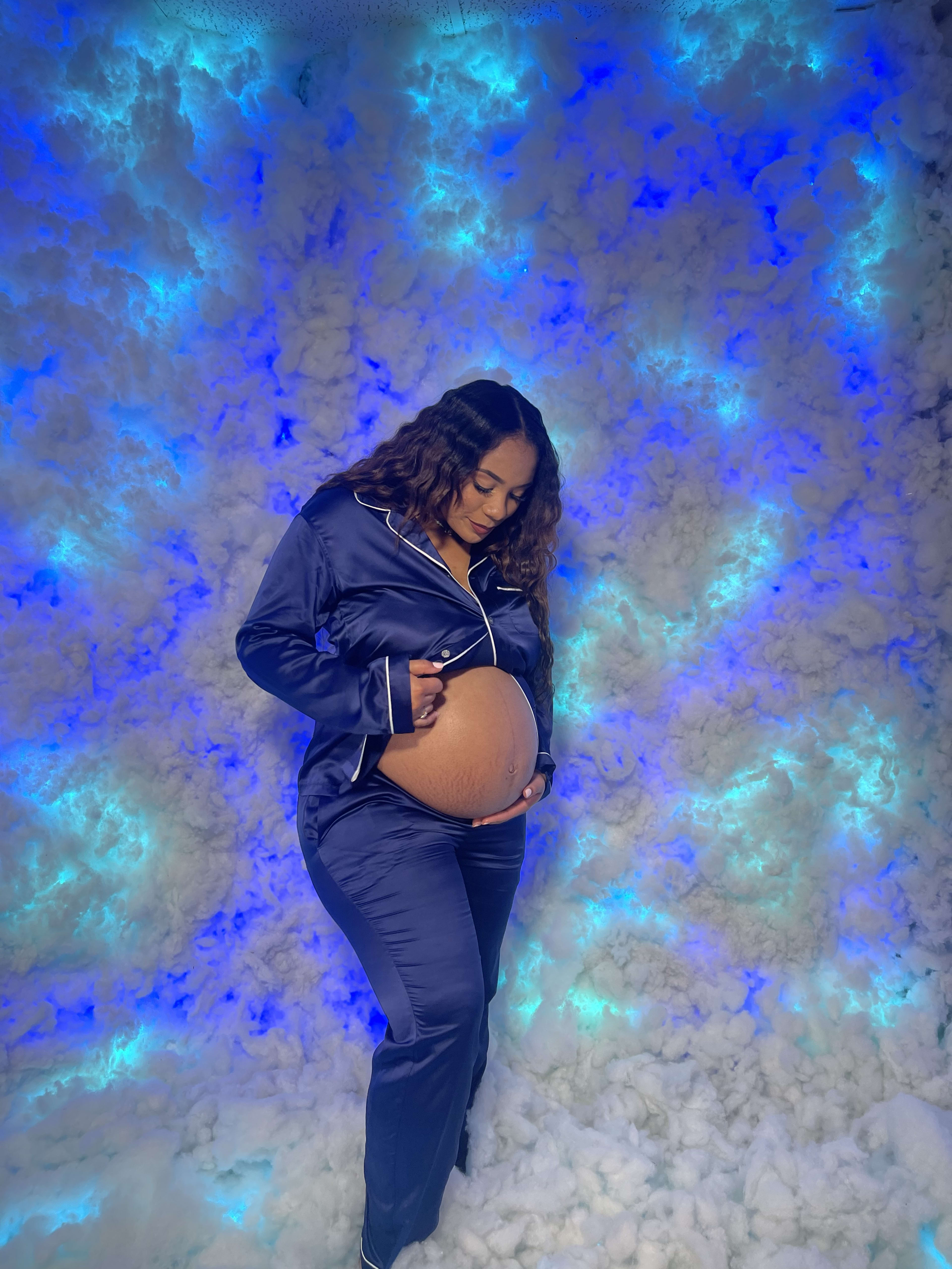 A maternity photoshoot with a woman posing next to blue clouds.