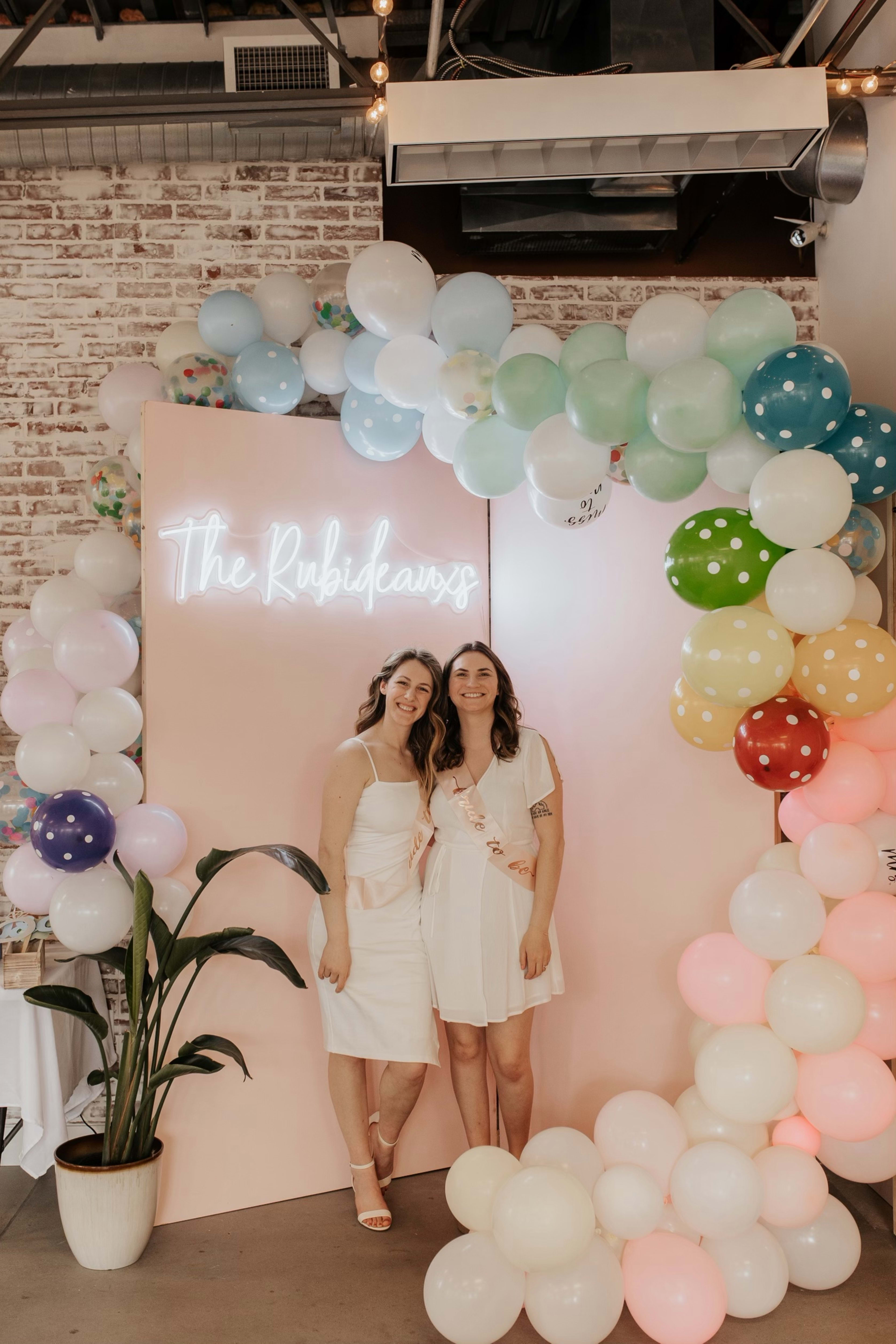 A couple of women standing next to each other in front of rainbow balloons.