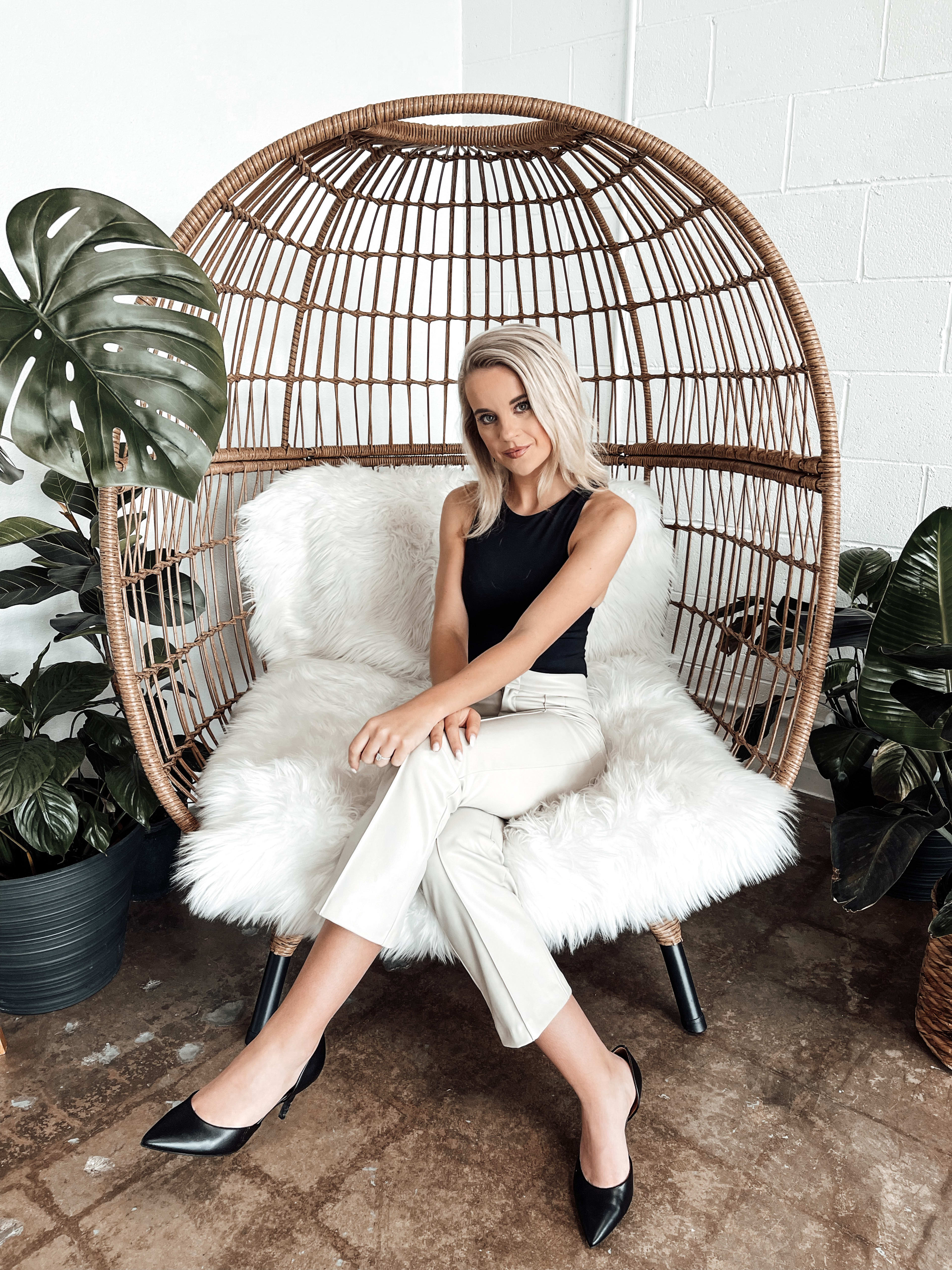 A woman sitting in a chair surrounded by green plants during a boho photoshoot.