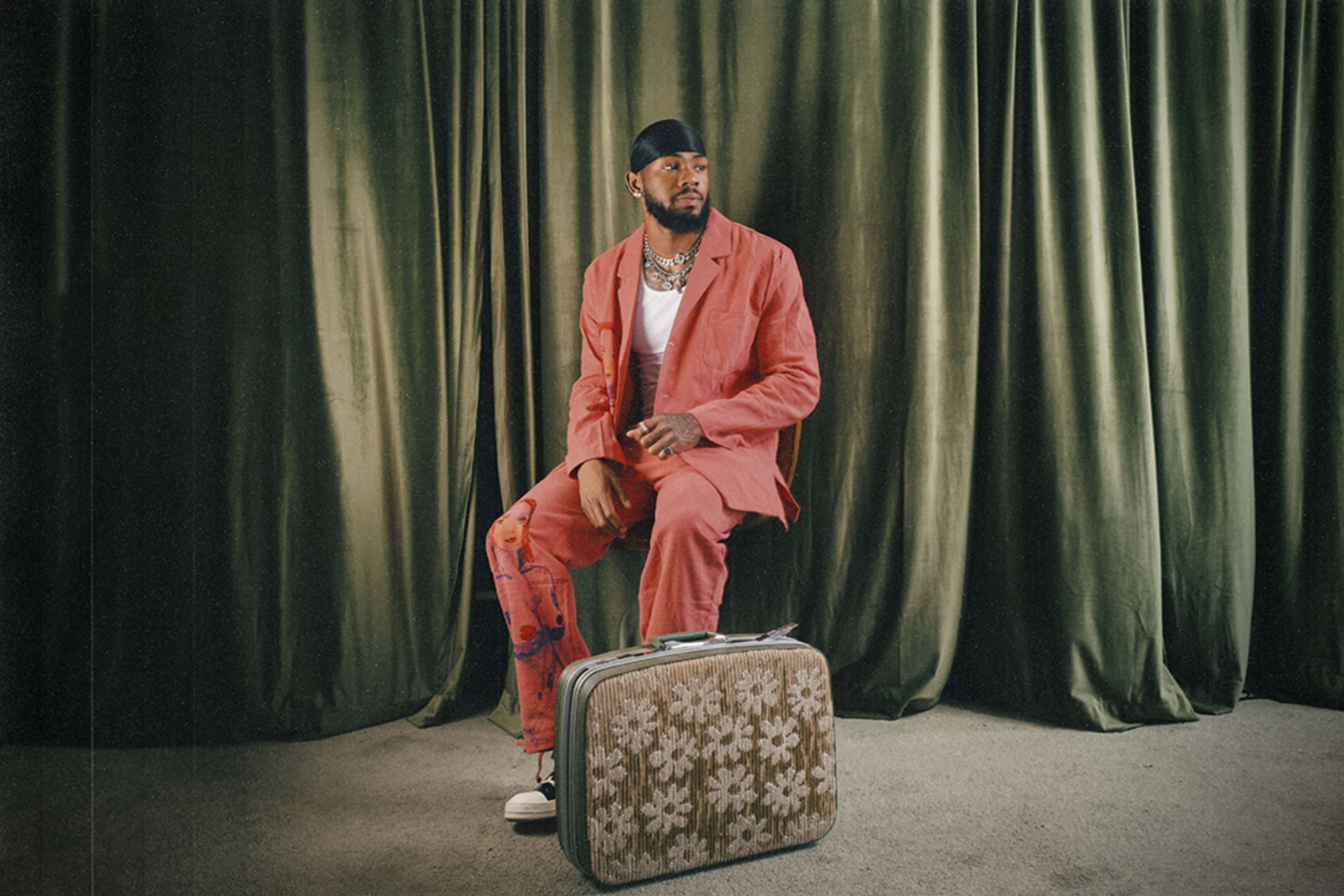 A man posing for a fashion photo shoot in front of a green curtain.