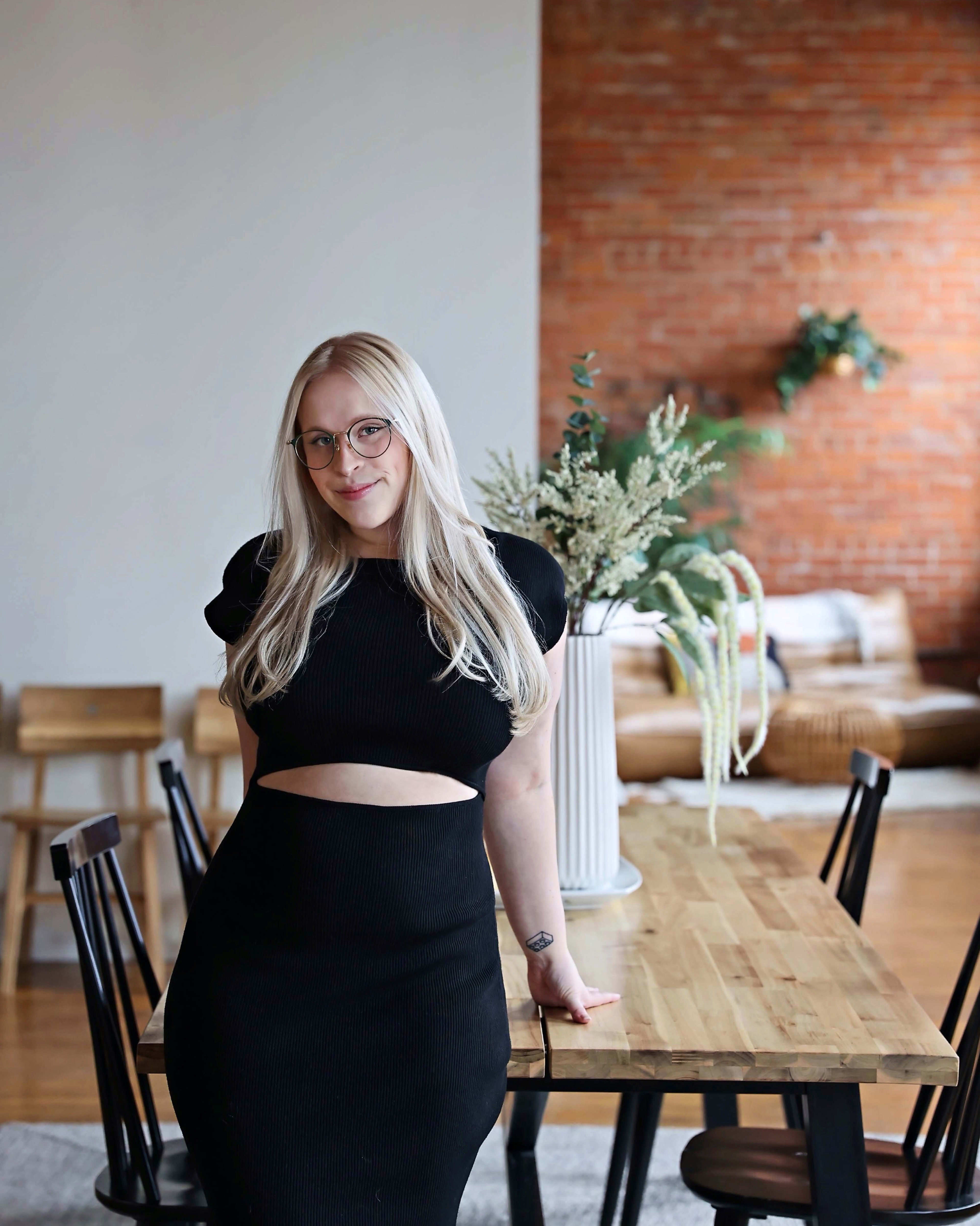 A rustic photoshoot featuring a woman posing in front of a wooden table showcasing a product.