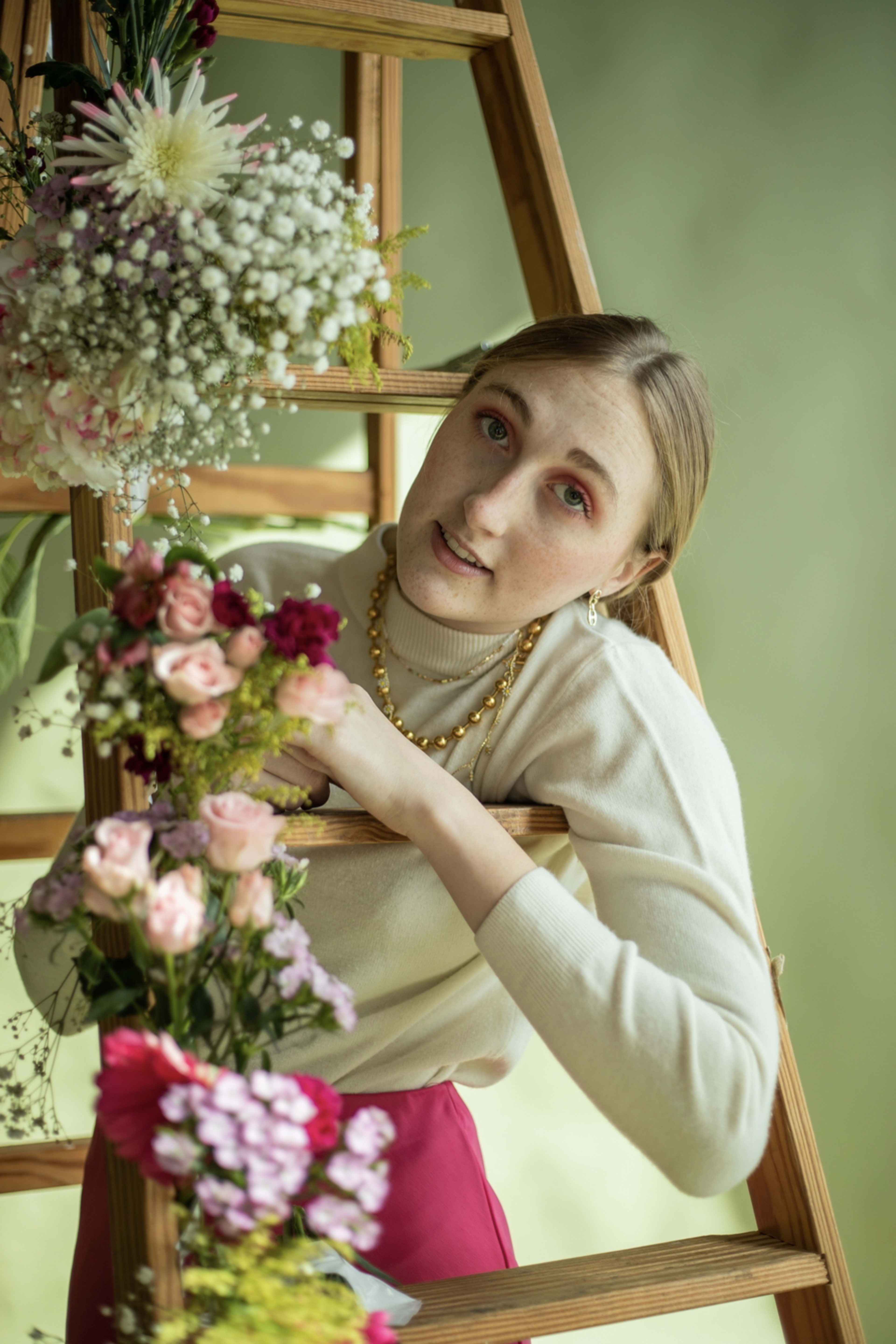 Una mujer apoyada en una escalera sosteniendo un ramo de flores.