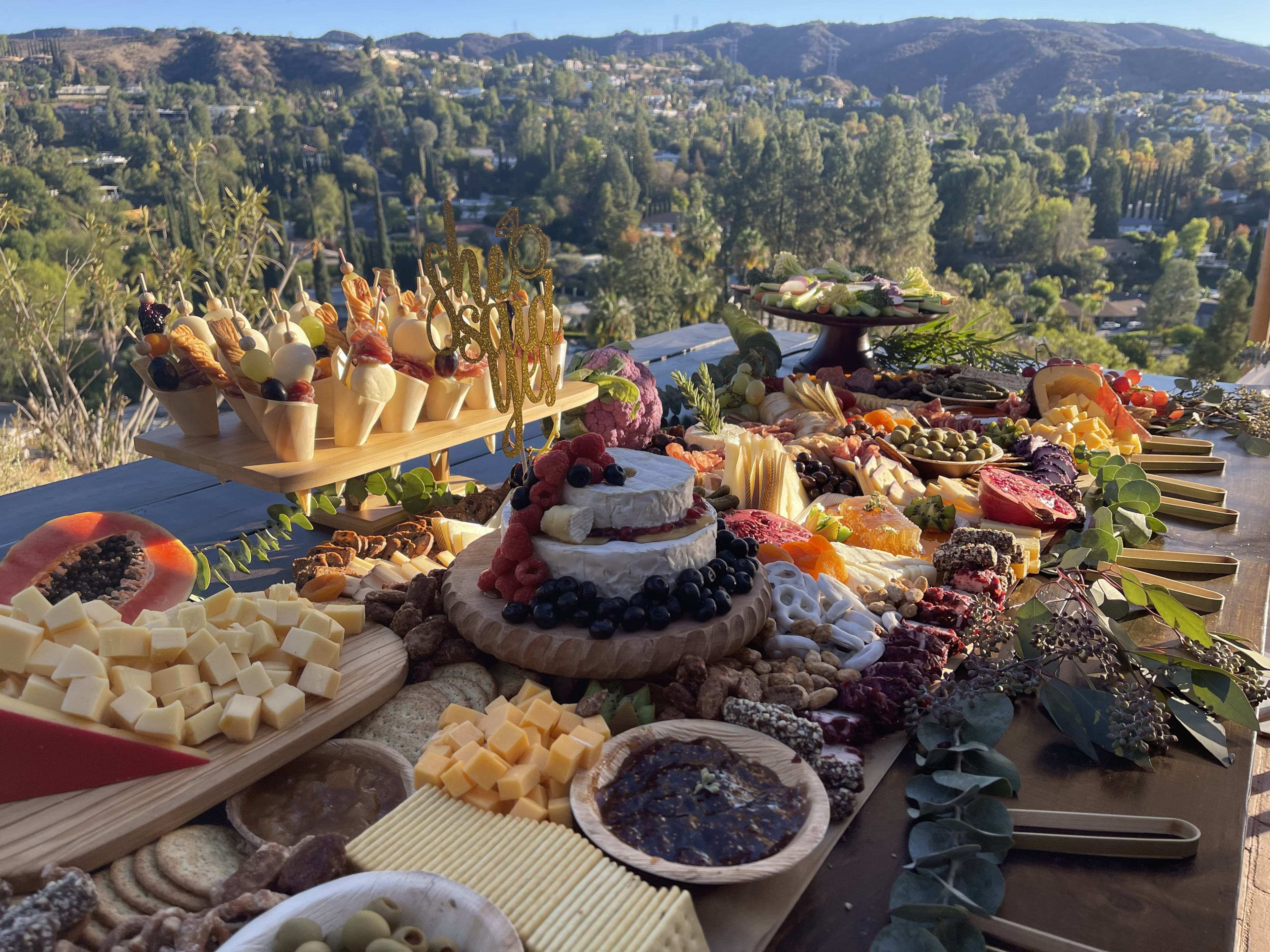 Auf einer Verlobungsparty im Freien wird eine Auswahl an Käse und Crackern auf einem Tisch ausgestellt.