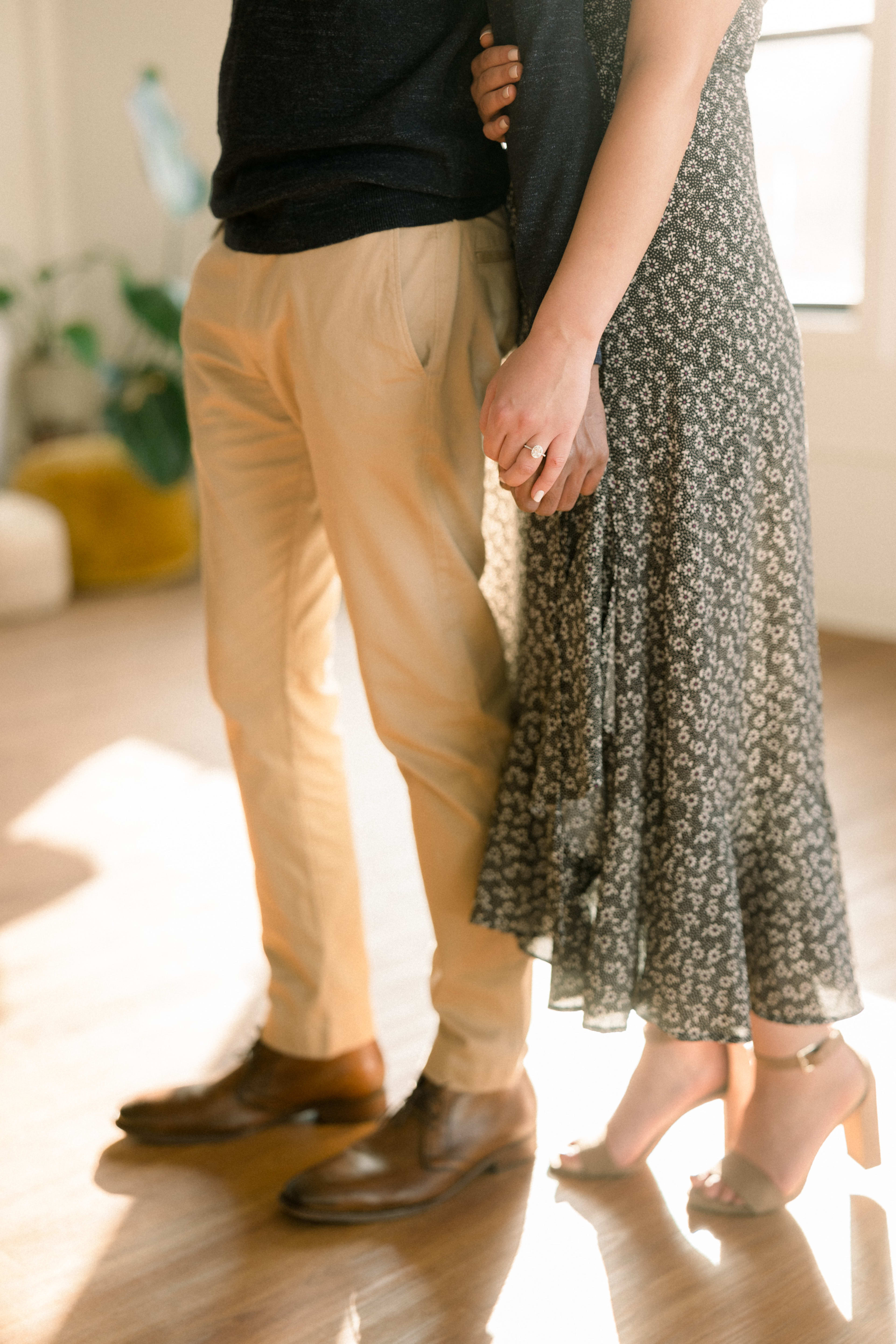 A couple standing on a wooden holding hands floor during an engagement photo shoot.