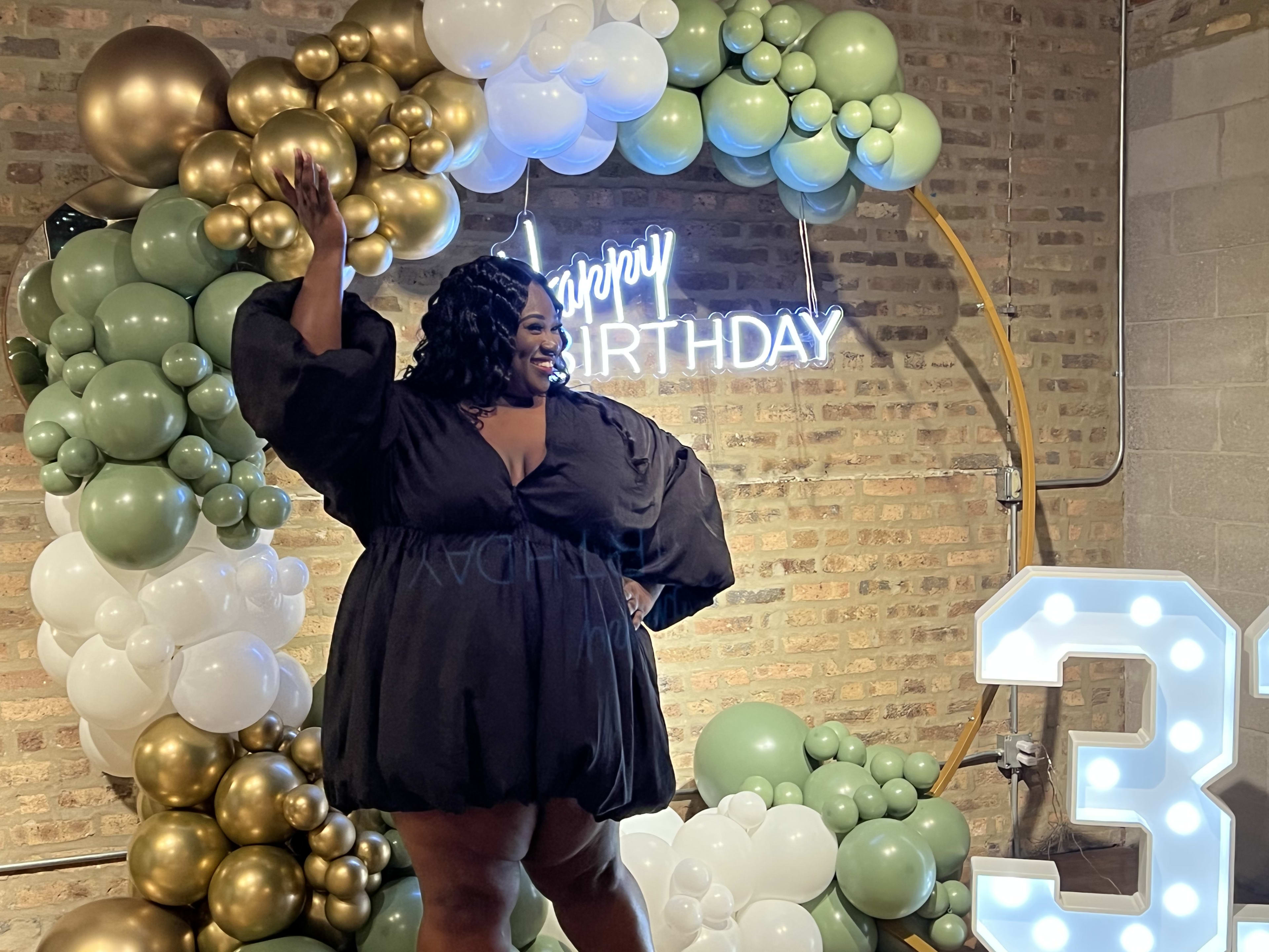 A woman in a black dress in front of balloons at a birthday party.