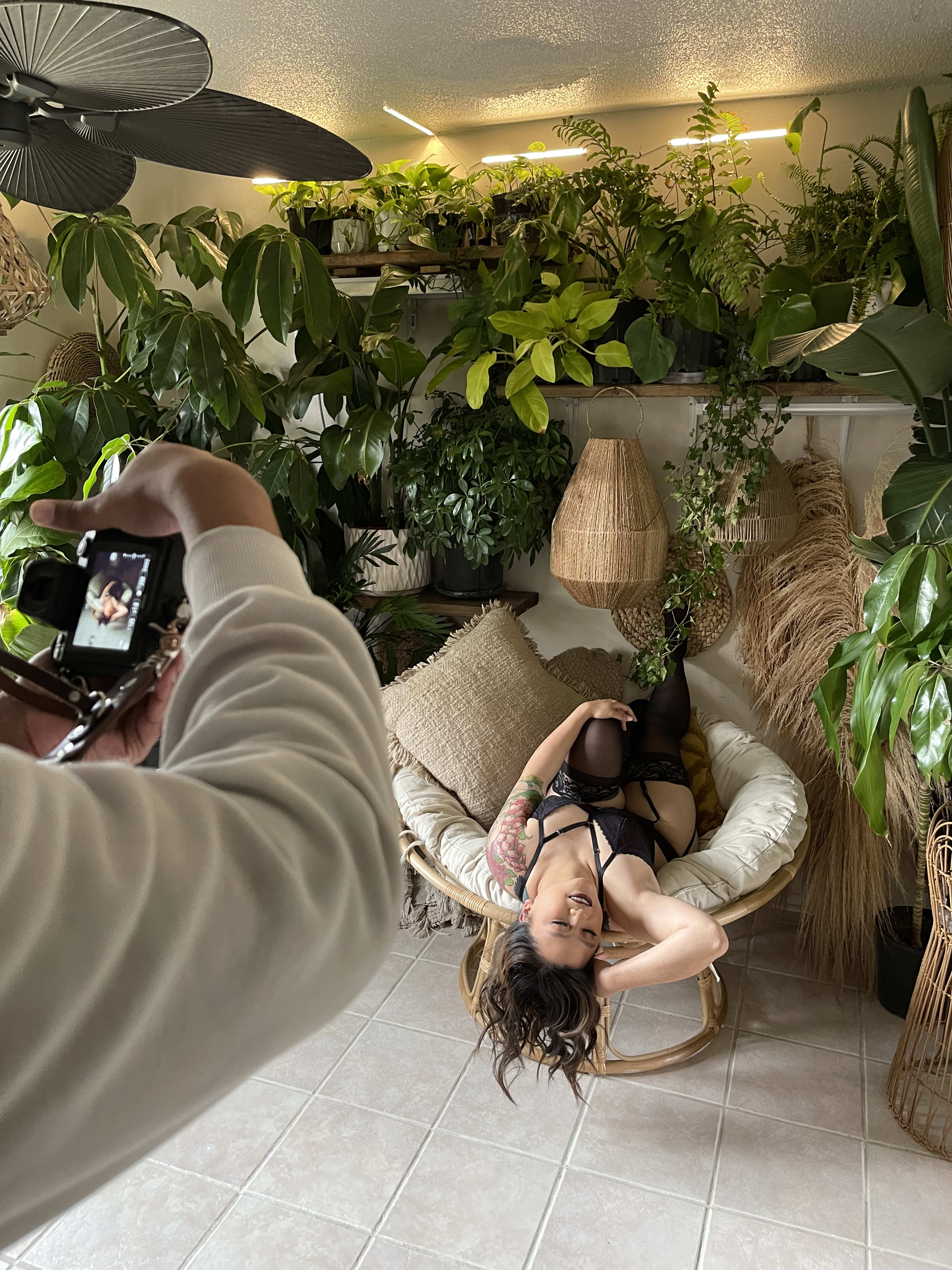 A woman is posing for a photo shoot in front of green plants.