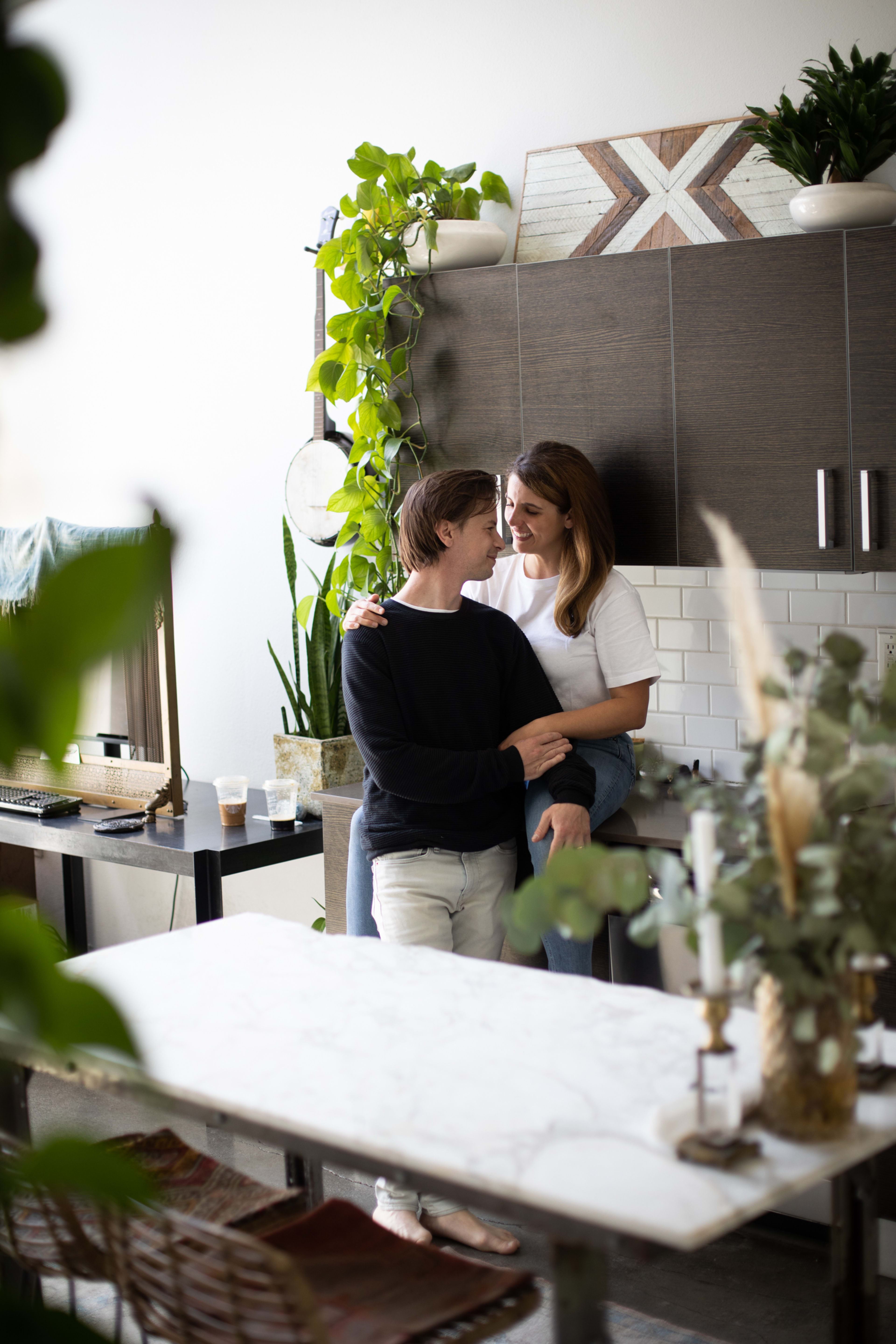 A couple embracing in a kitchen surrounded by plants.