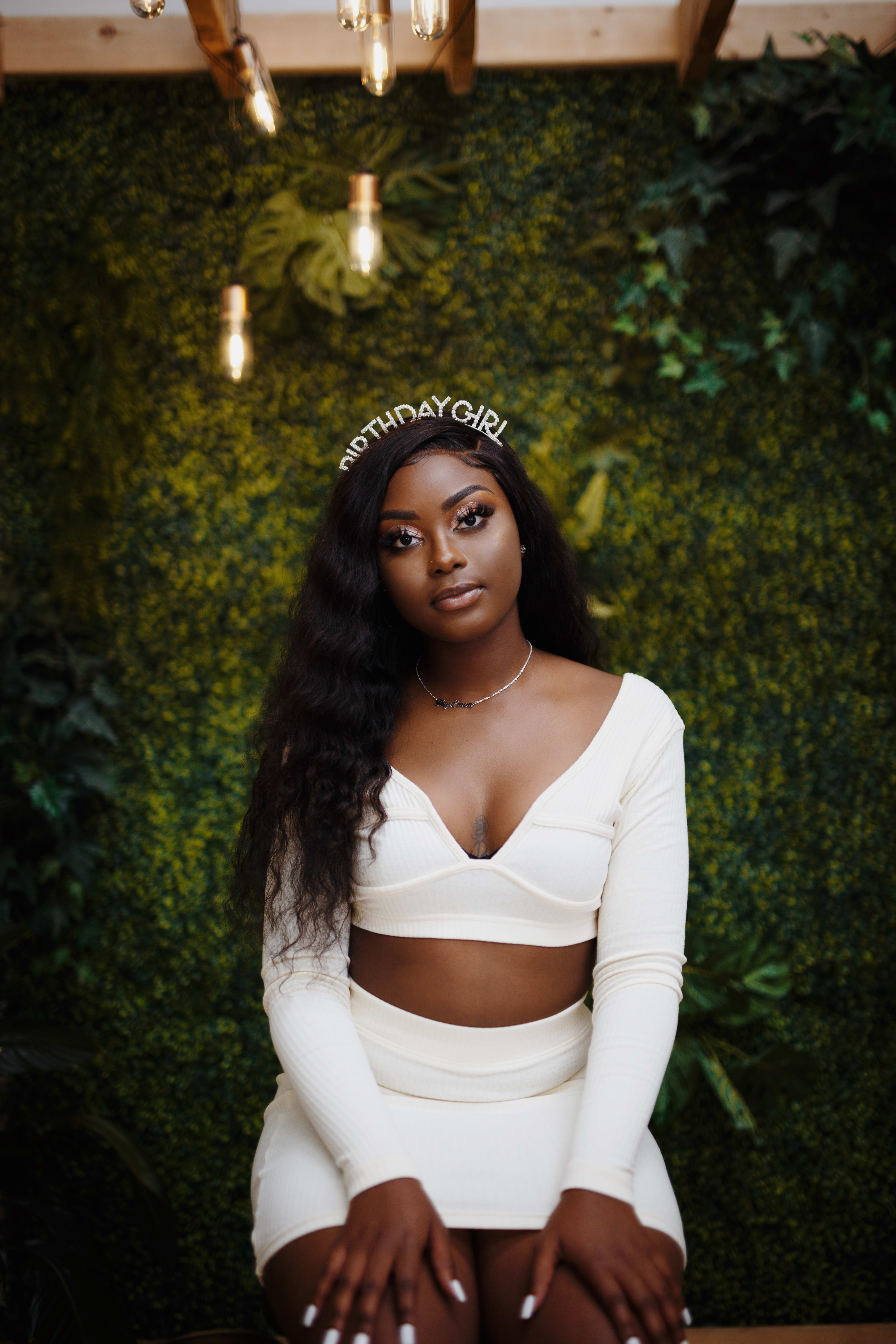 A woman sitting on a table in front of a green wall during a photo shoot.