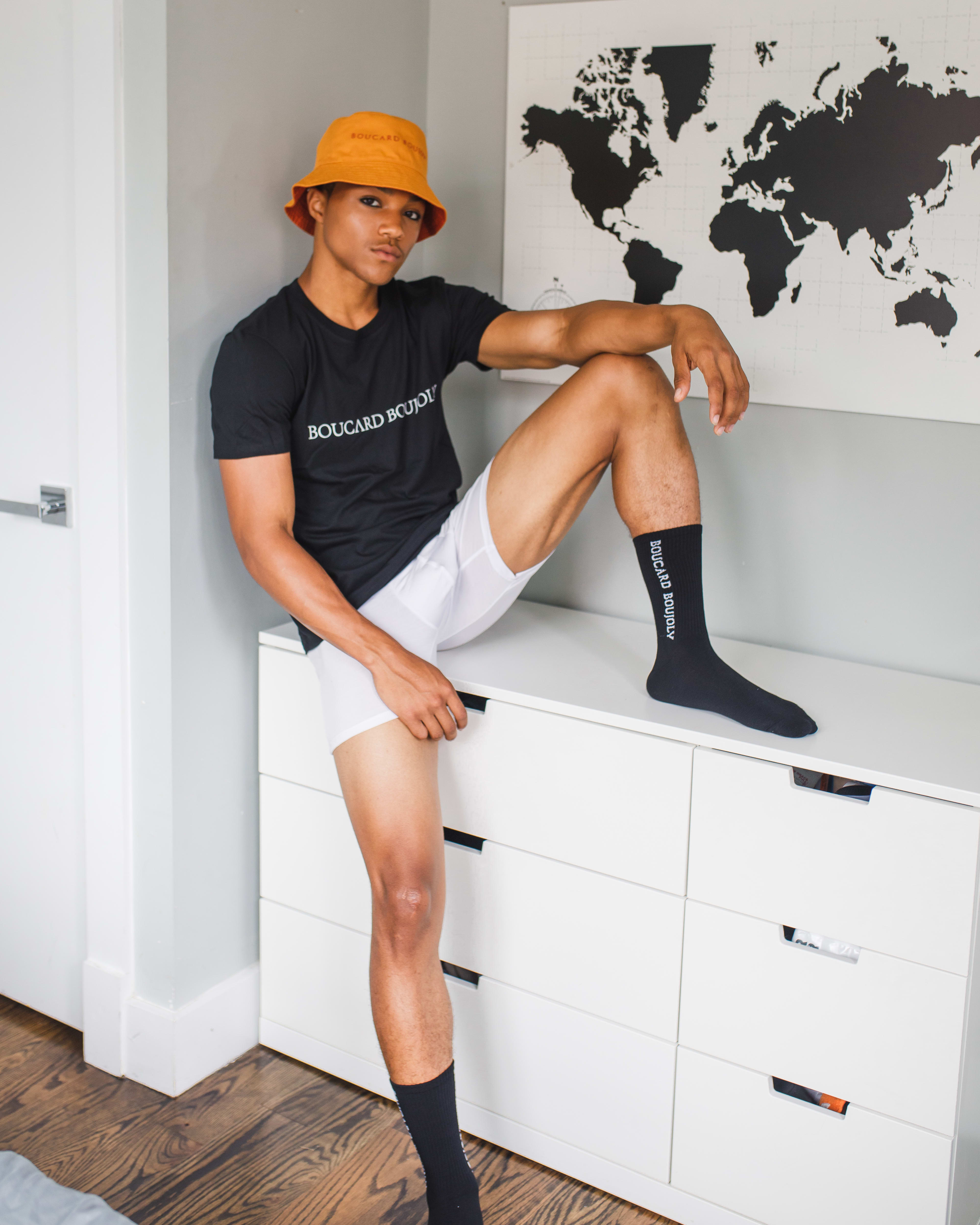 A man posing on a white chest of drawers for a black and white photo shoot.