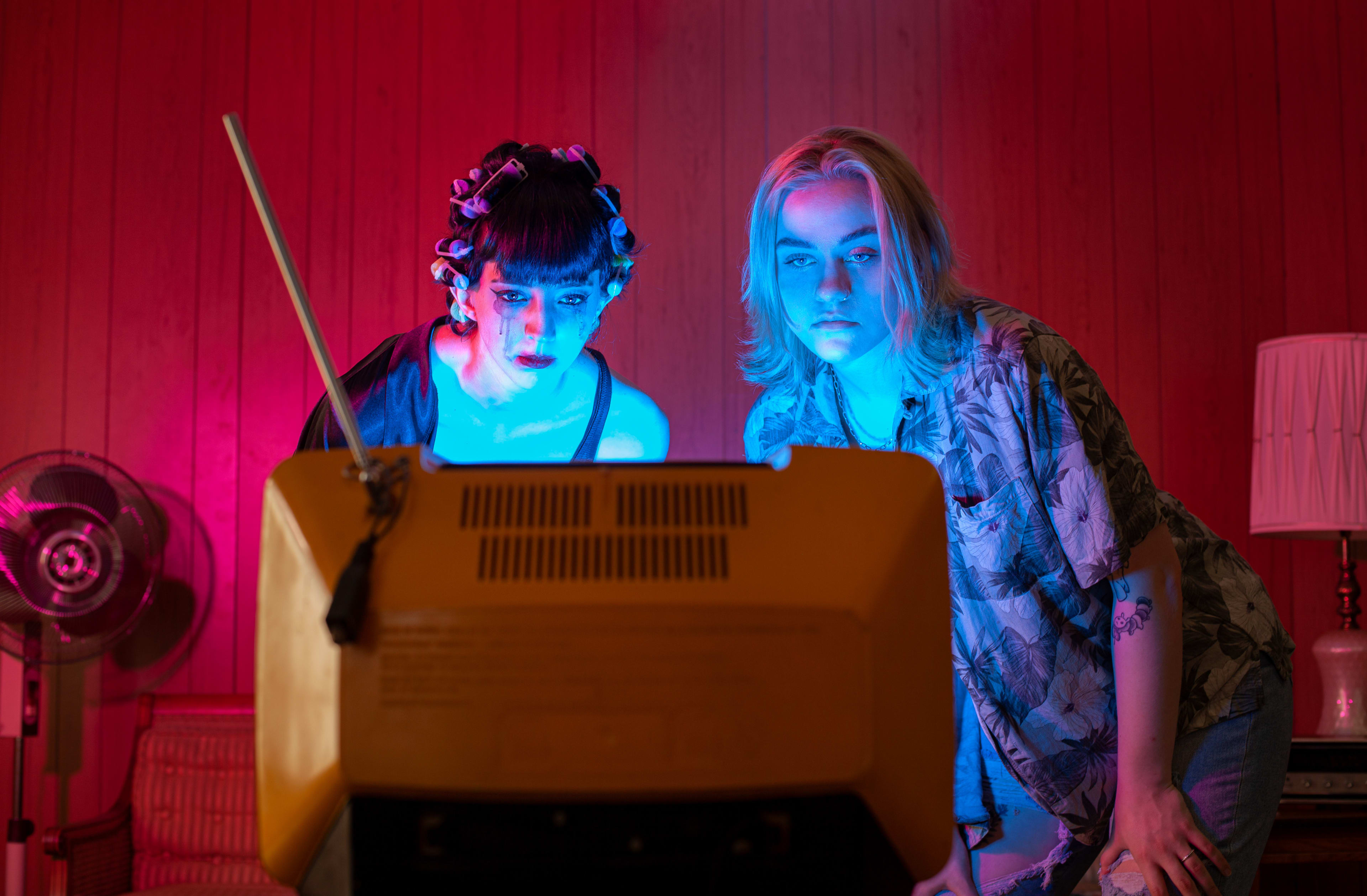 Dos mujeres posando delante de un televisor durante una sesión de fotos retro.