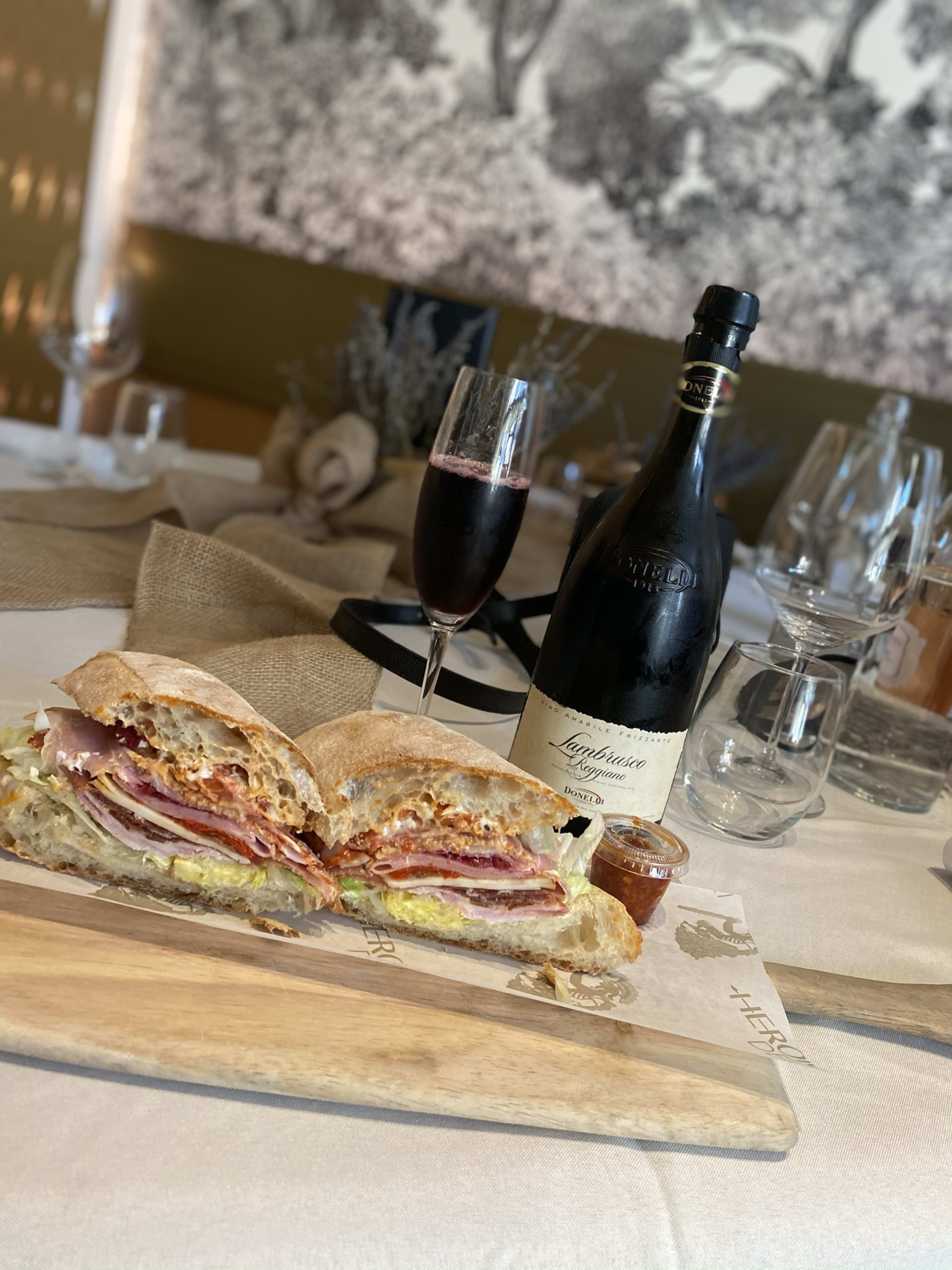 A sandwich on a cutting board next to a glass a red wine.