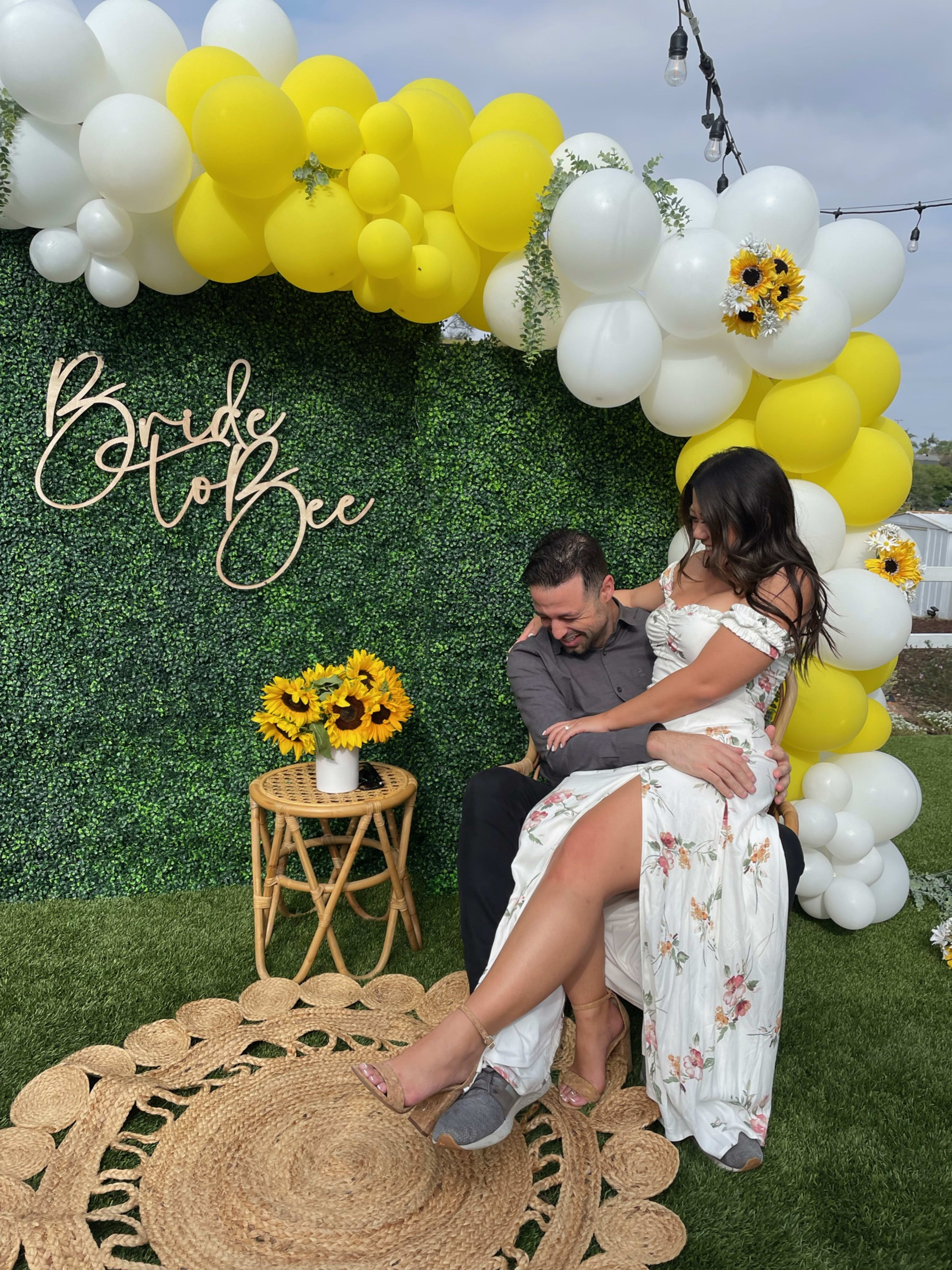 A couple sitting on a mat under a  boho yellow and white balloon arch.