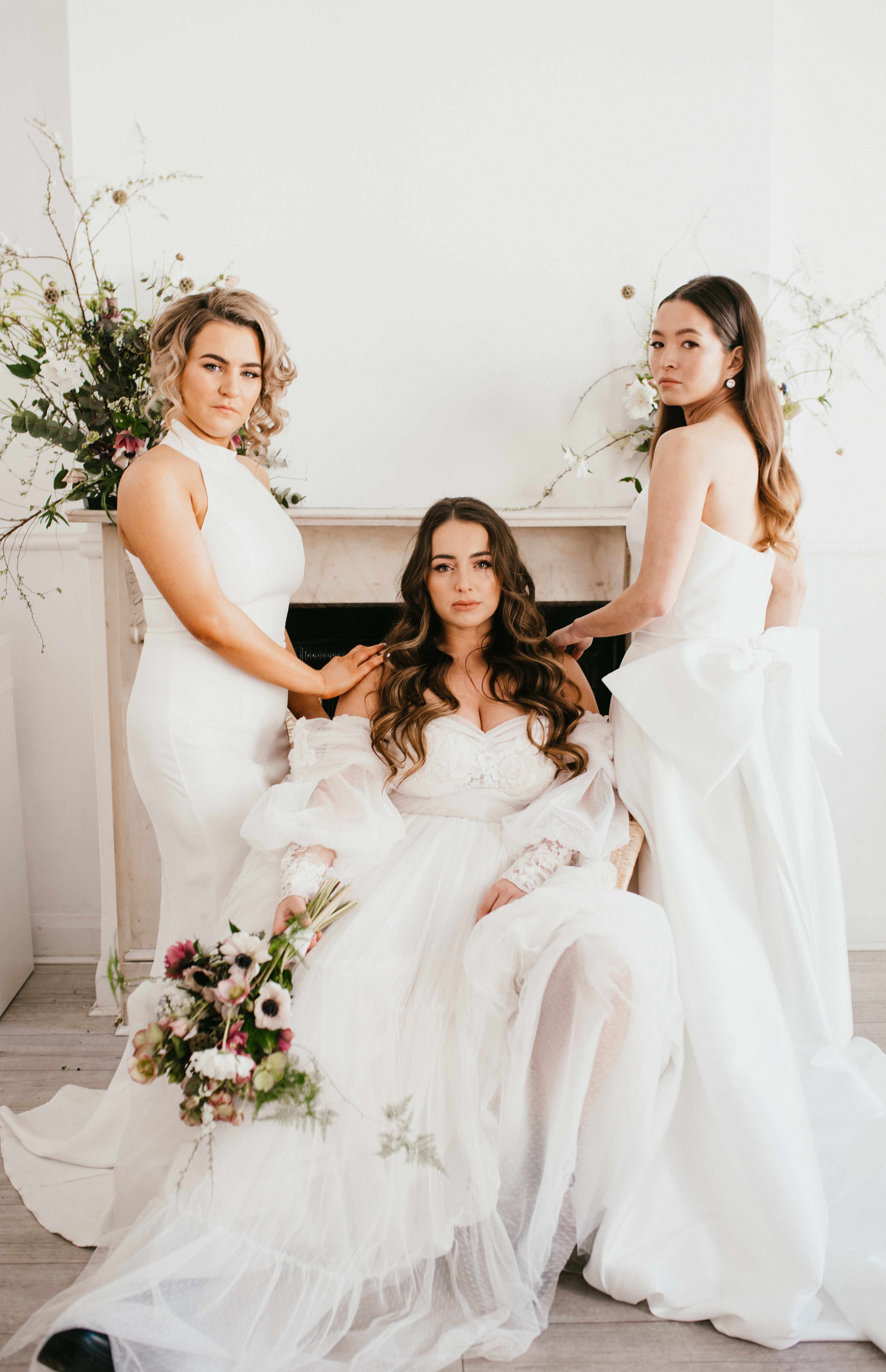 Una sesión de fotos nupcial con las damas de honor frente a una chimenea blanca rodeada de flores.