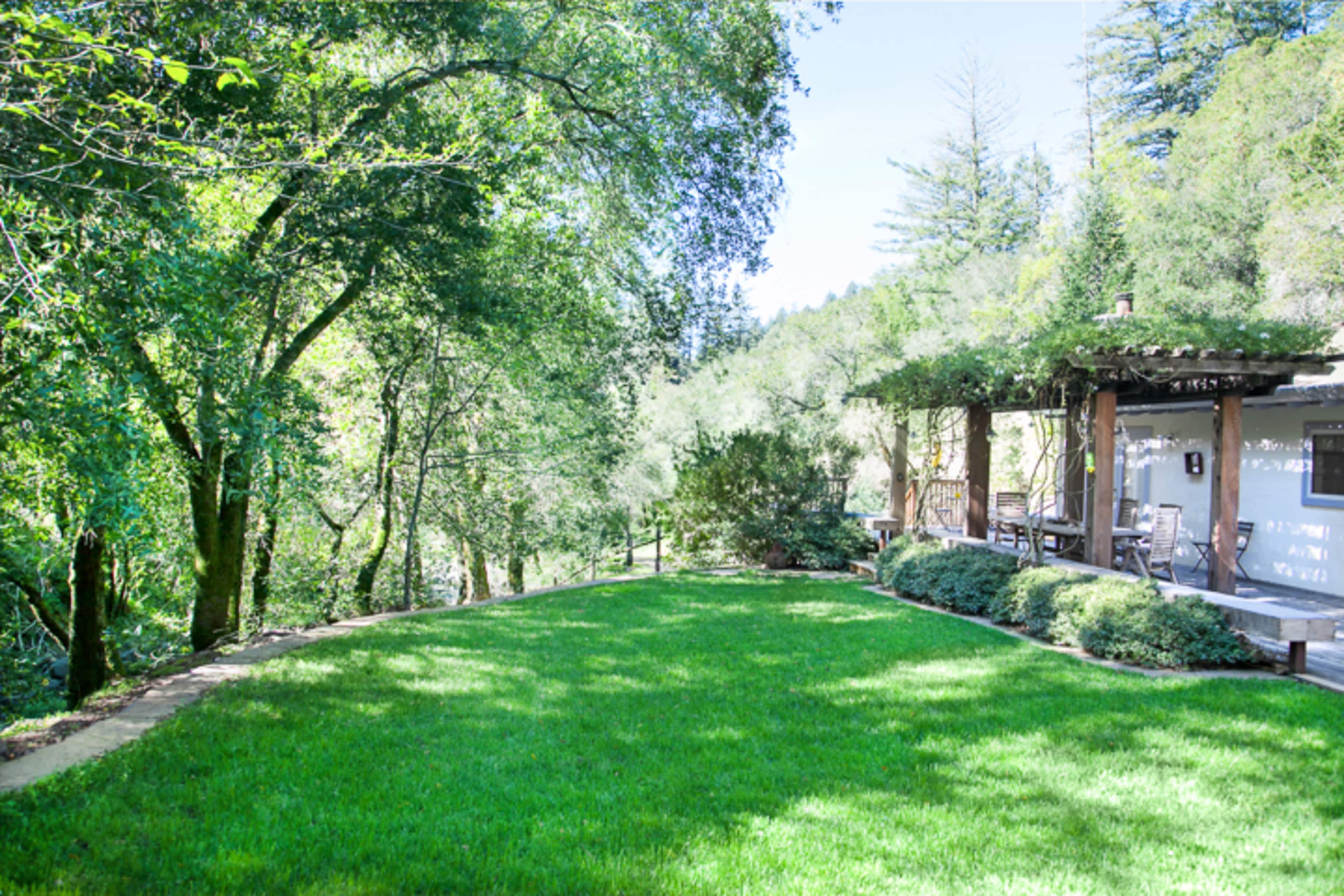 A lush green lawn bordered by trees, leading up to a wooden patio.
