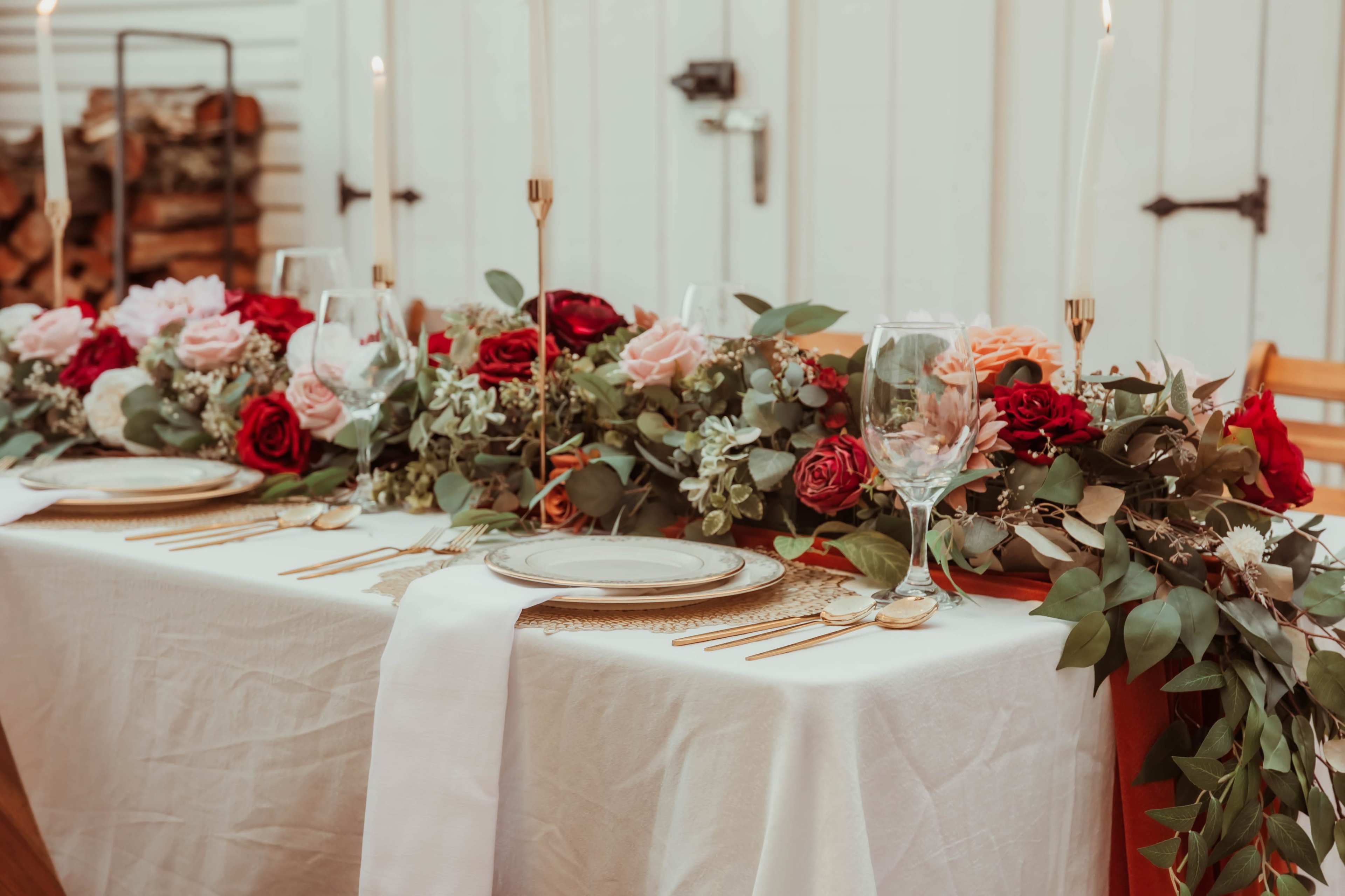 A long dining table is set with elegant glassware, flatware, and a decorative arrangement of roses and greenery.