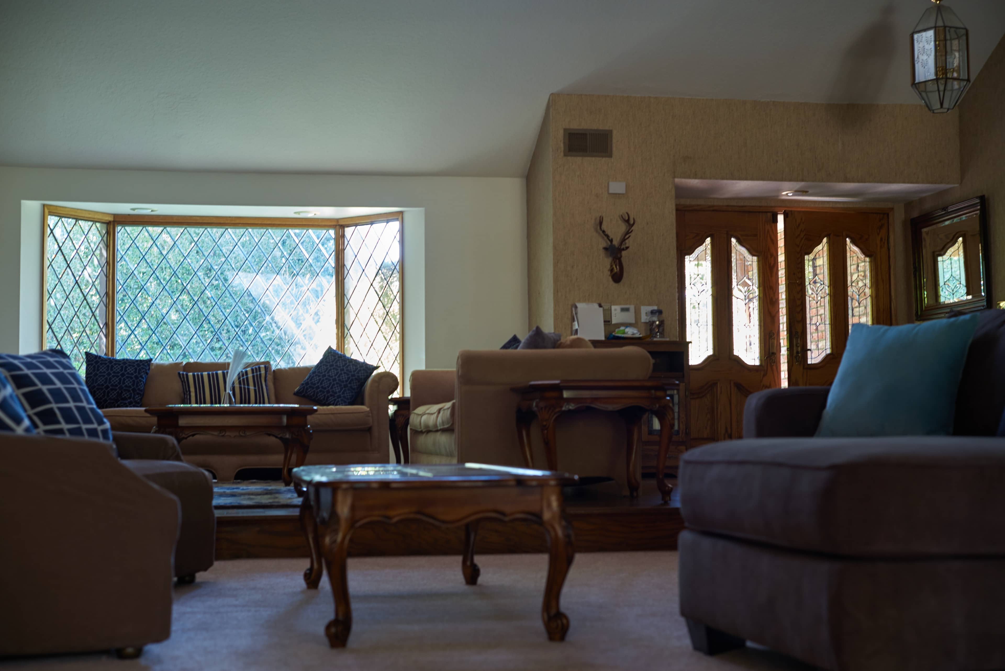 A spacious living room features a variety of seating arrangements, a wooden coffee table, and large windows with diamond-patterned panes.