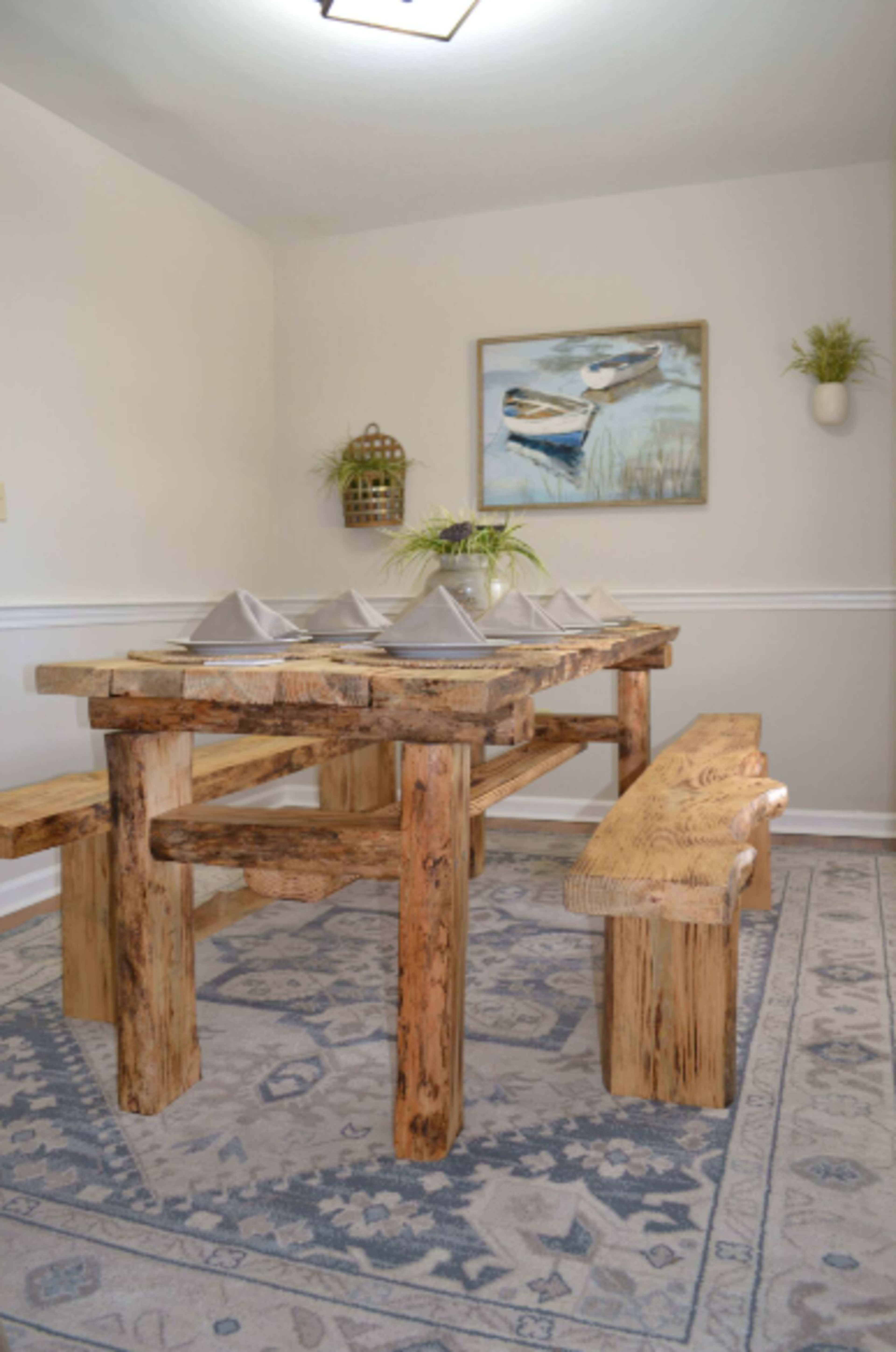 A rustic wooden dining table is set with cloth napkins, surrounded by matching benches in a well-lit room.