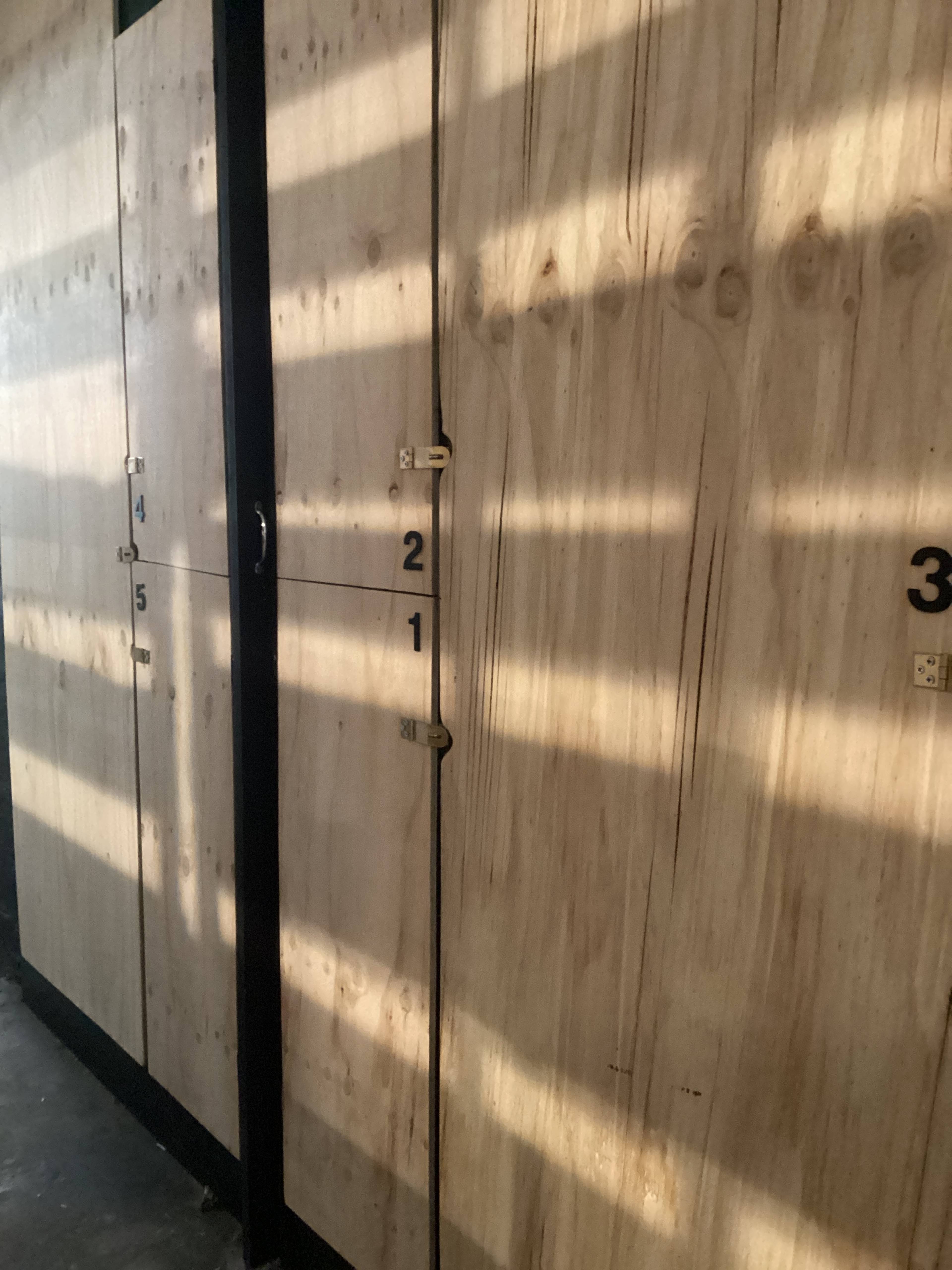 The image shows a series of wooden storage lockers numbered 1 through 5, with natural light casting shadows on the surface.