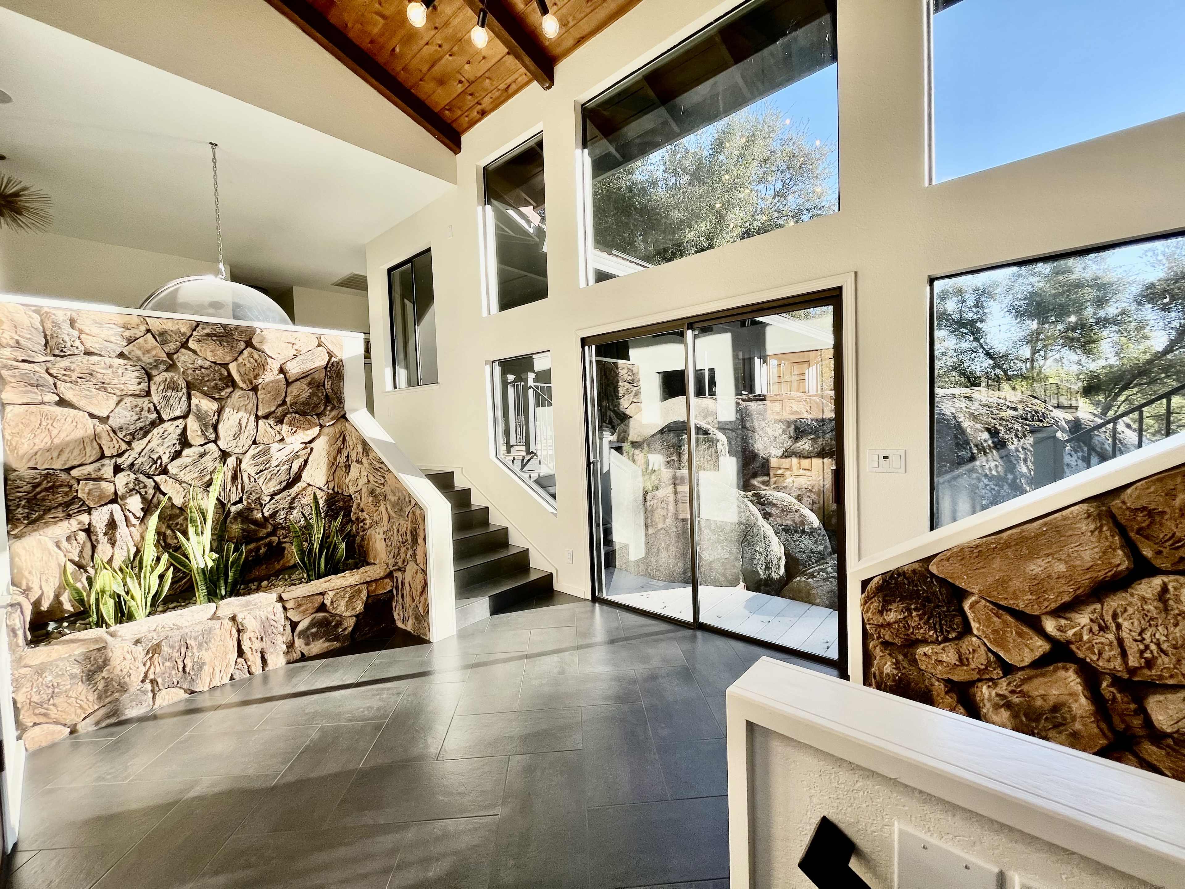A modern entryway with stone walls, large windows, and a staircase leading to an upper level.