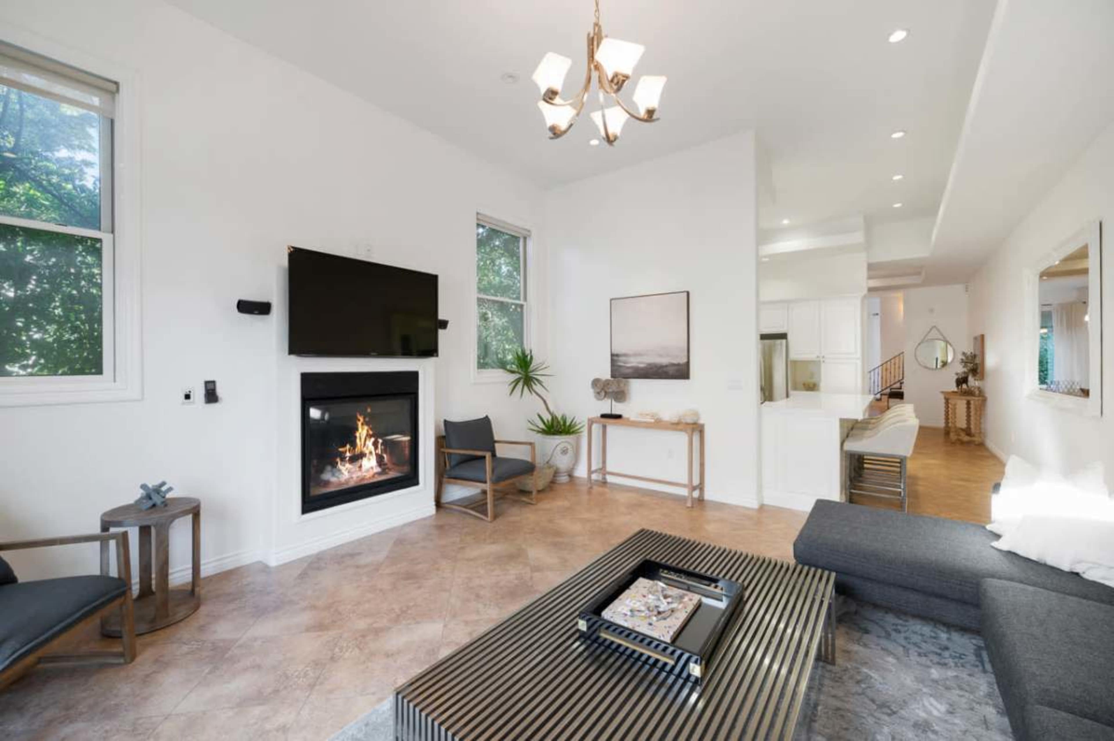 The image shows a modern living room with a fireplace, a flat-screen TV mounted on the wall, a coffee table, and minimalist furniture.