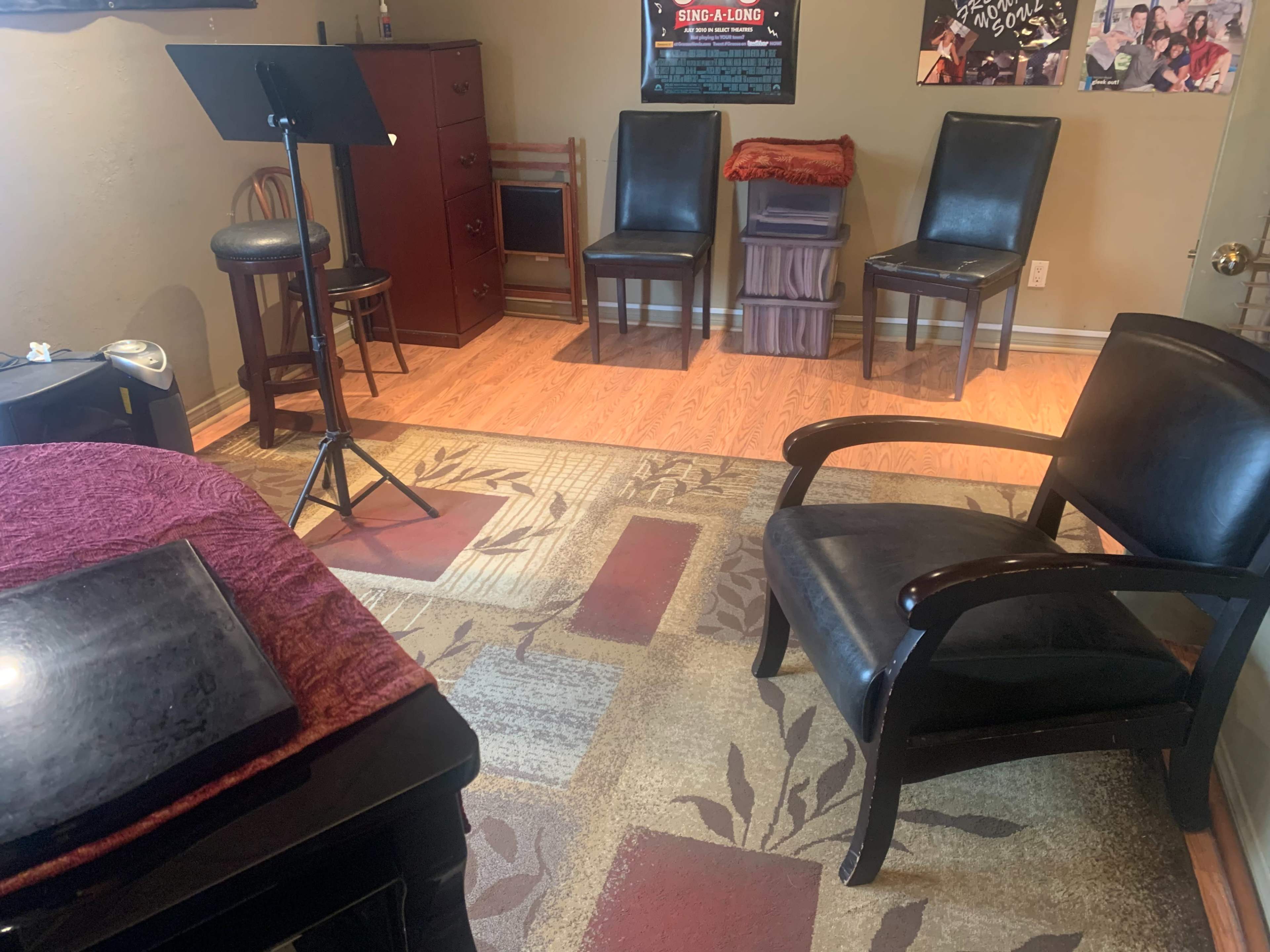 The image shows a room with a wooden floor, a microphone stand, several chairs, and a small table.