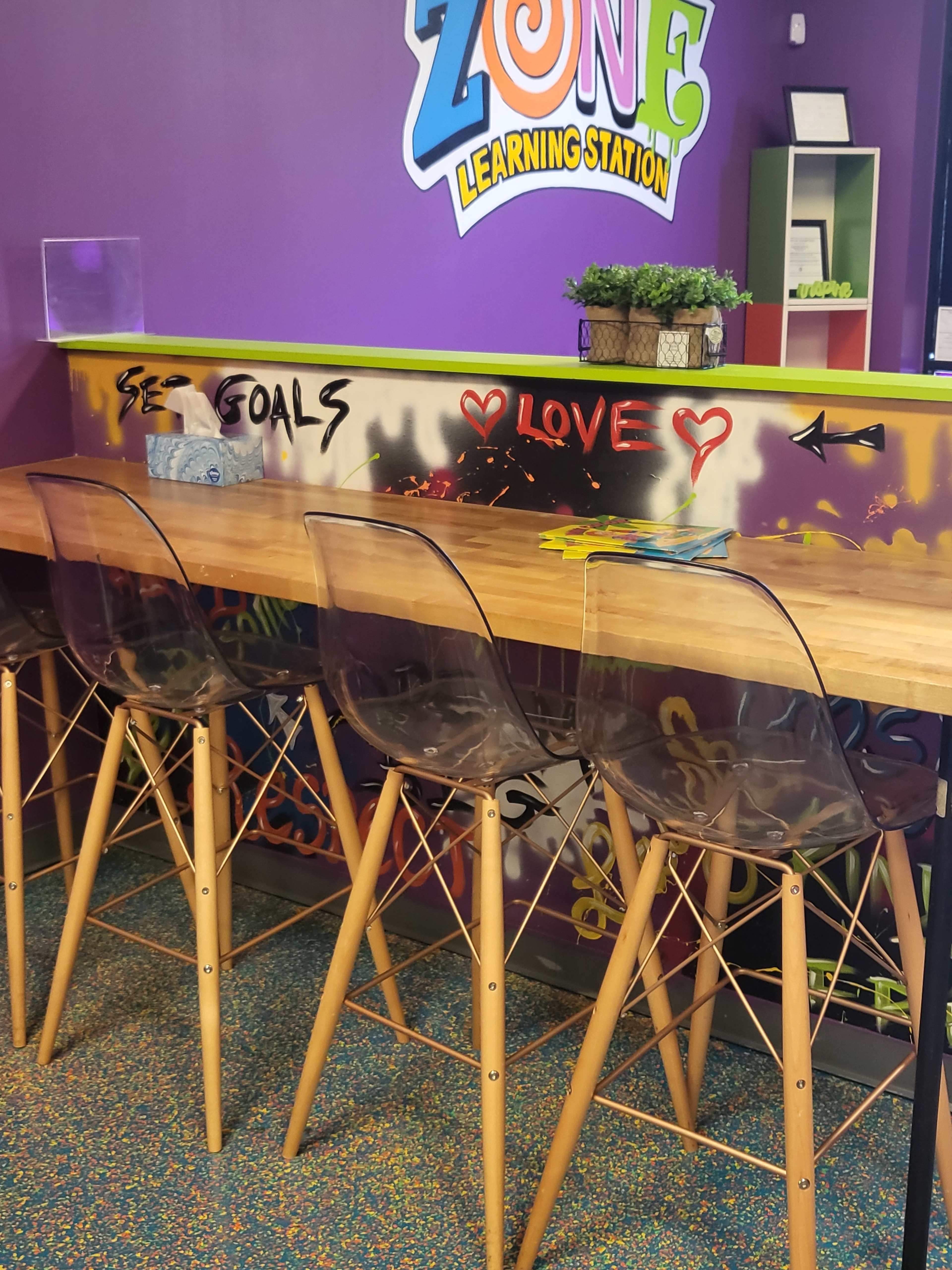 A colorful learning station with a wooden bar table and transparent chairs against a graffiti-style wall.