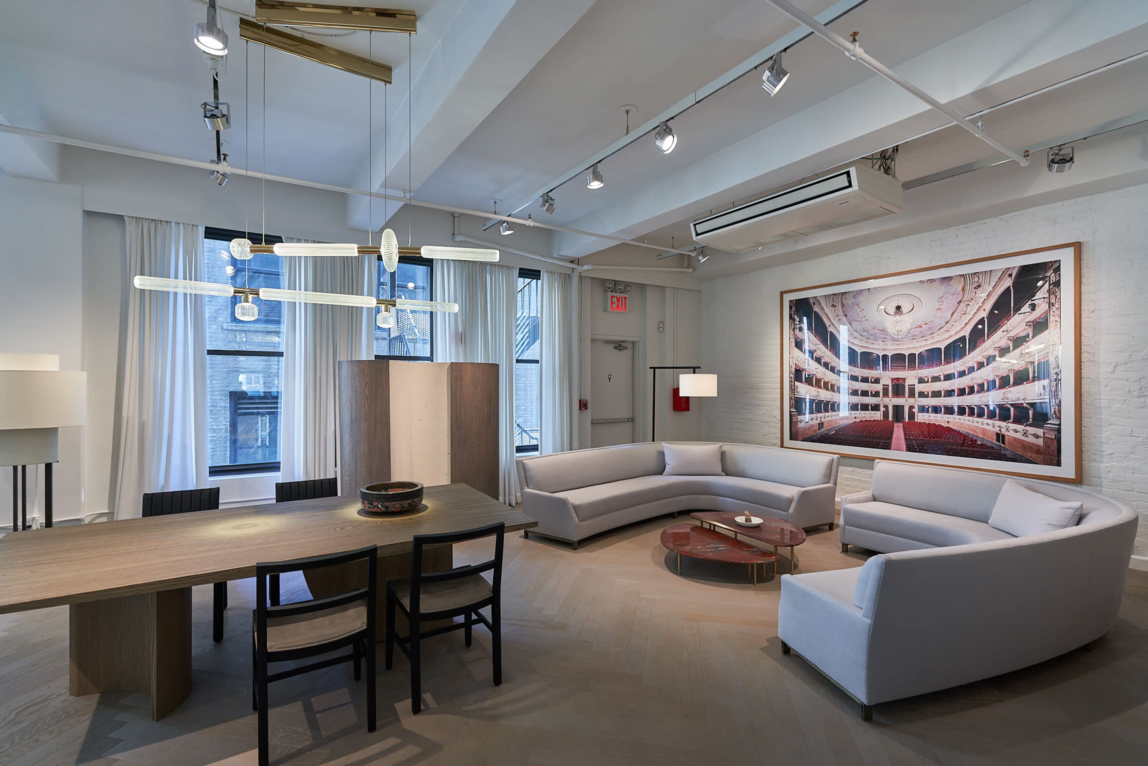 A modern living space features a curved sectional sofa, a large dining table, and a striking wall art piece depicting an interior theater.