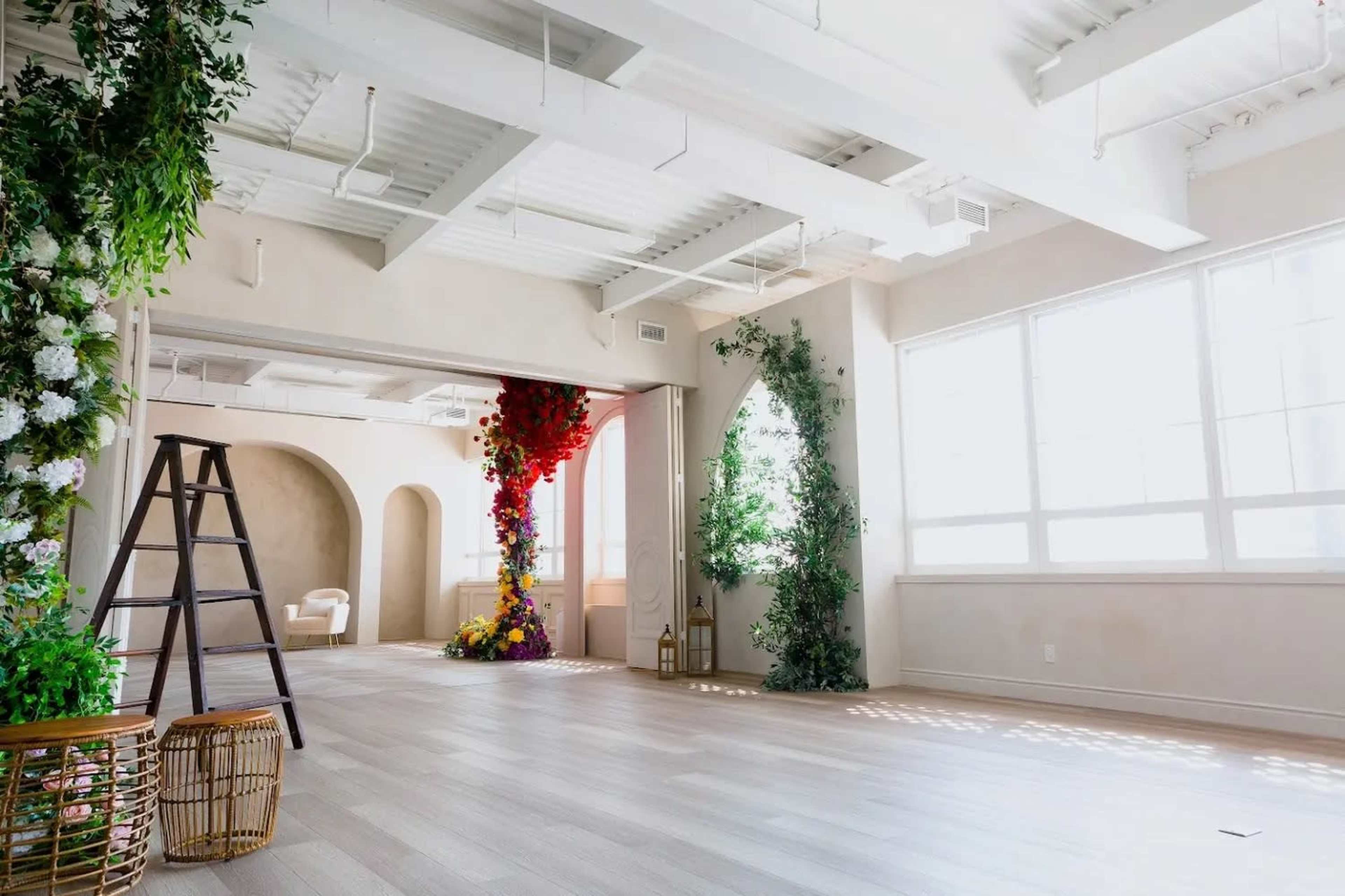 A bright, modern interior space with large windows, decorated with floral arrangements and a ladder positioned in one corner.