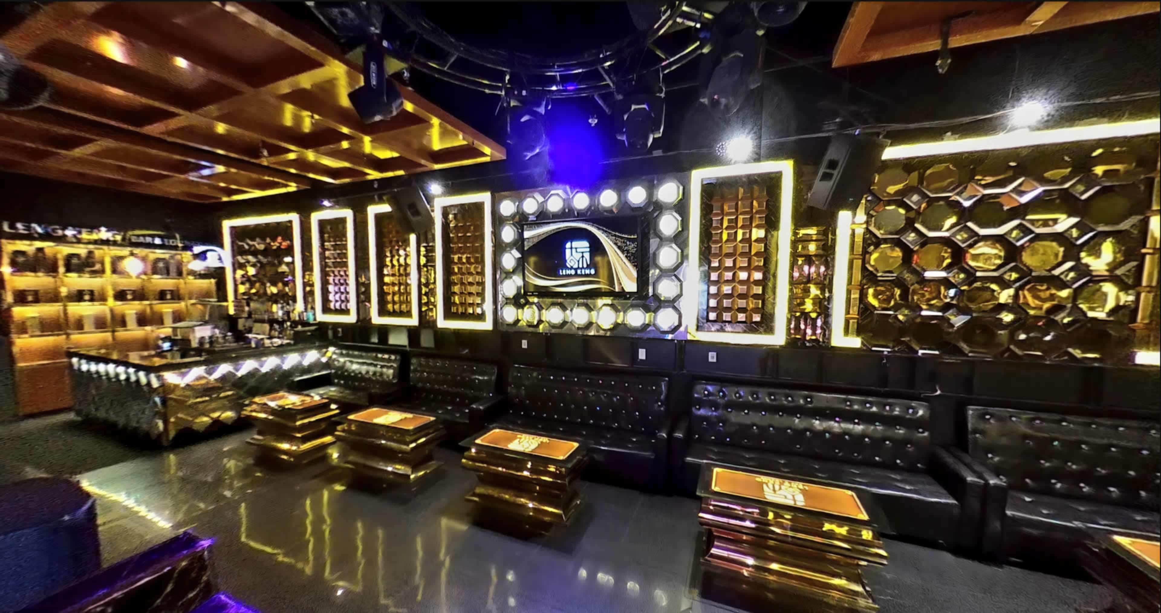 A modern lounge with black leather seating, illuminated gold accents, and a large screen framed by decorative panels.