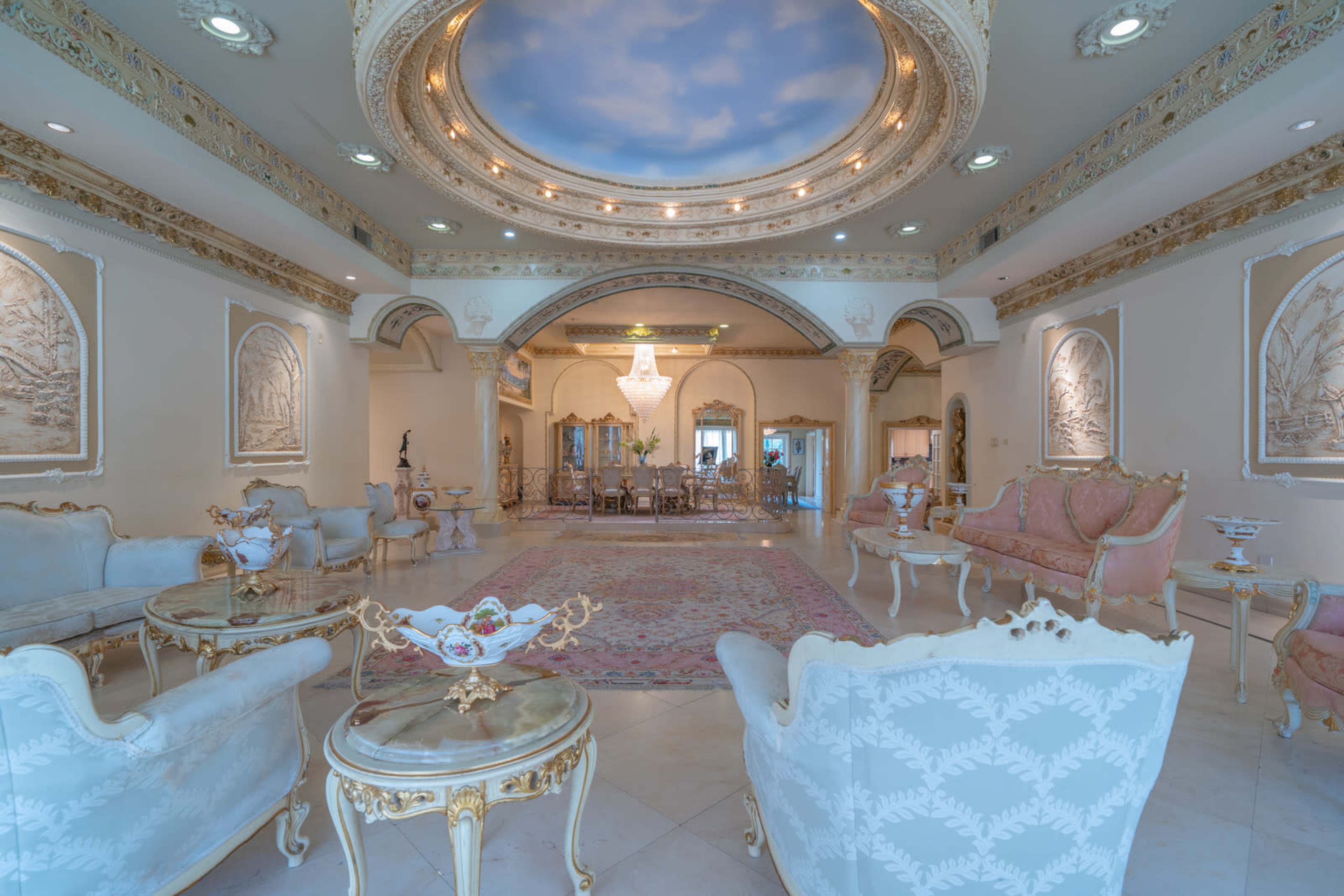 The scene depicts an ornate living room with elegant furniture, intricate moldings, and a large chandelier, complemented by a view of a sky mural on the ceiling.