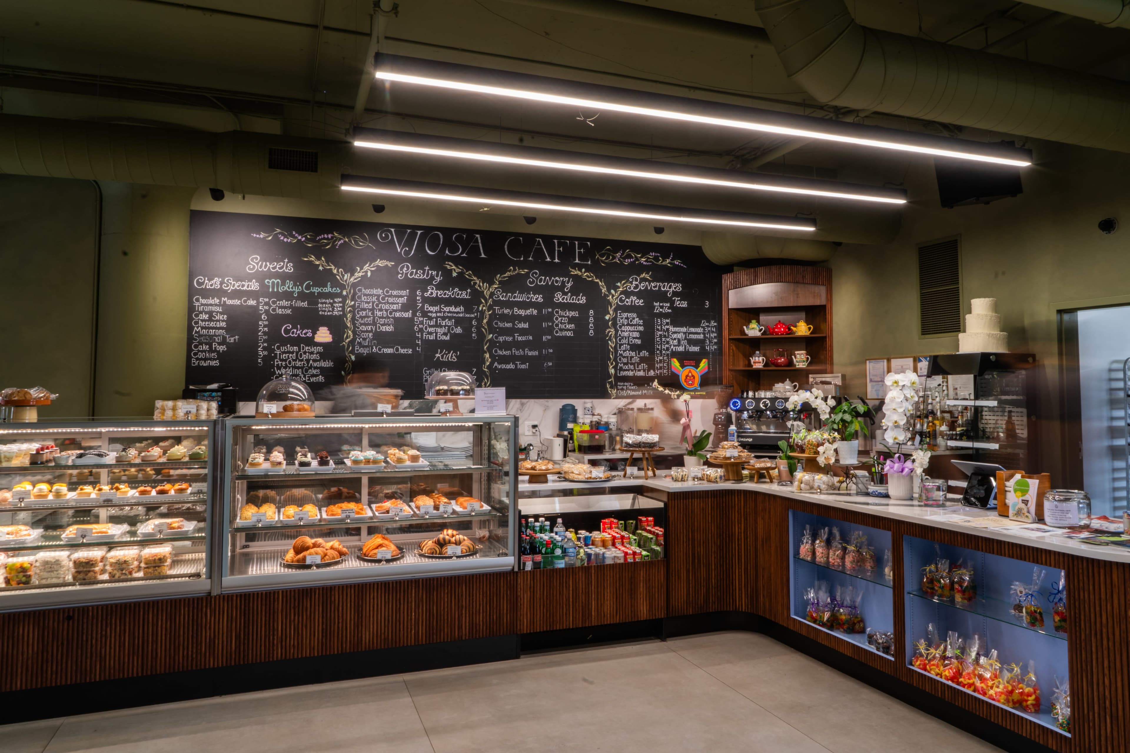 A modern café displays an array of pastries and beverages behind glass cases, with a menu written on a chalkboard wall.