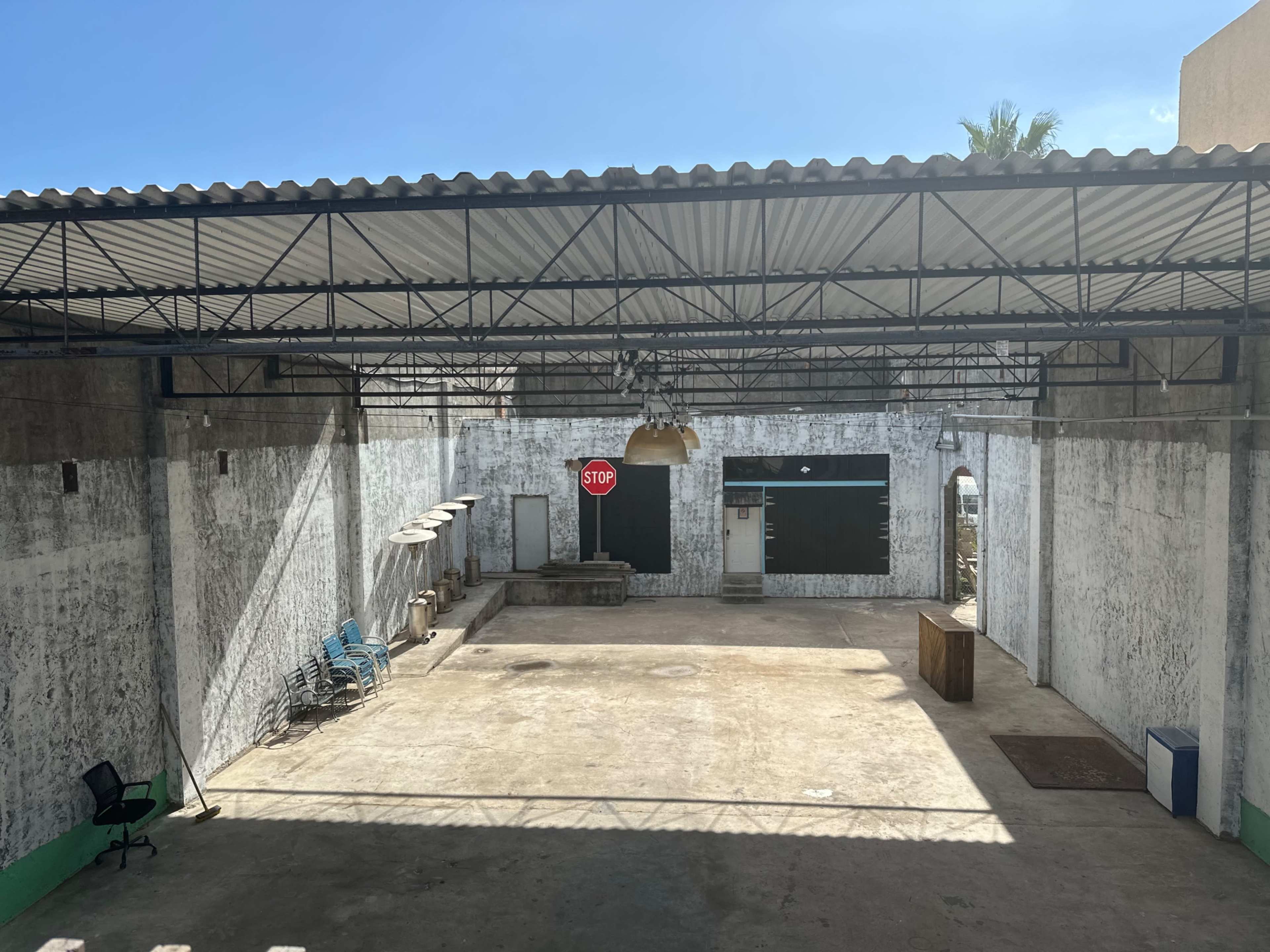 The image shows a large, empty industrial space with a concrete floor, whitewashed walls, a "STOP" sign, and a few pieces of furniture along the perimeter.