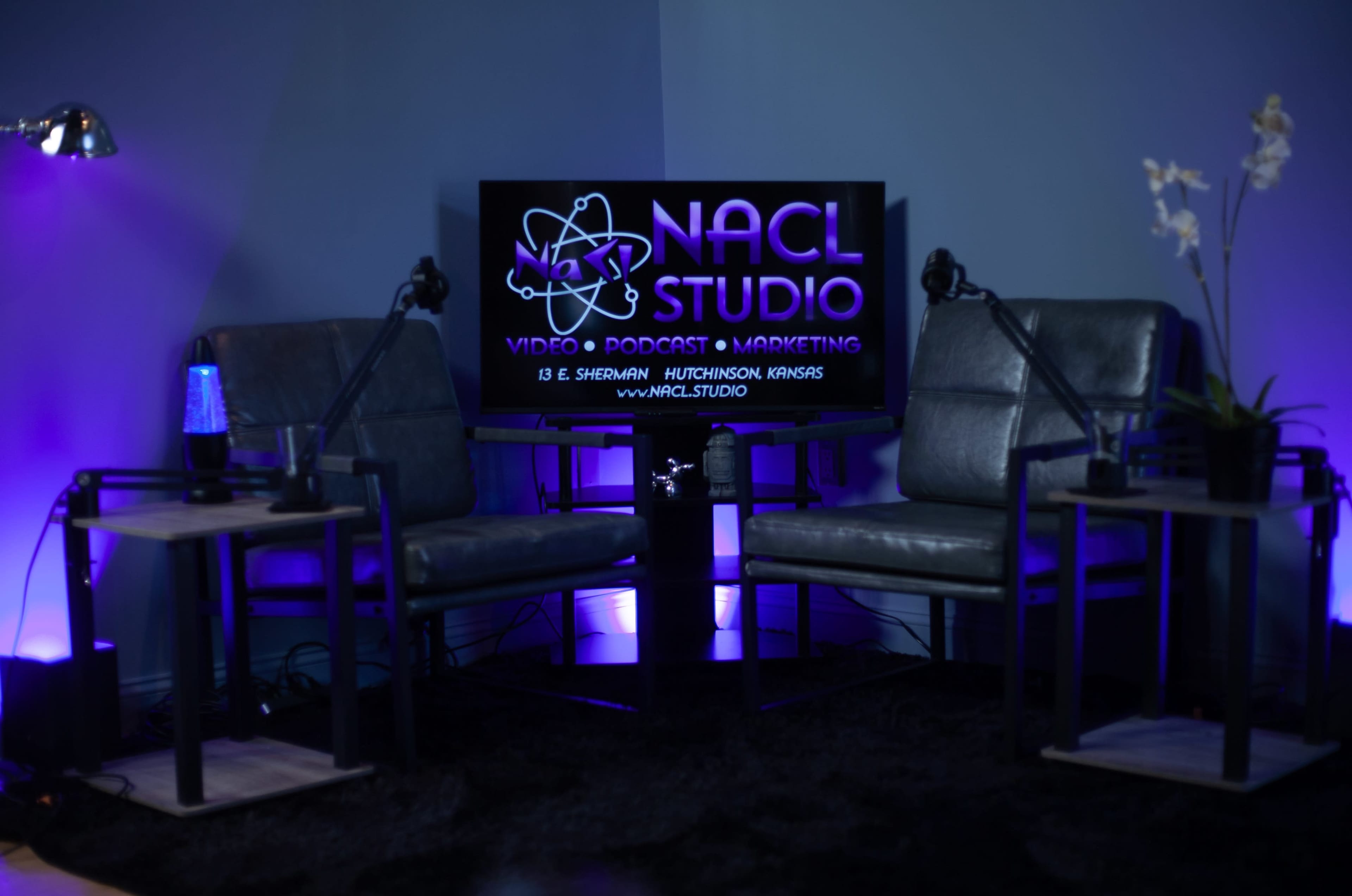 A modern studio setting features two gray chairs facing a screen that displays "NACL STUDIO" along with its services.