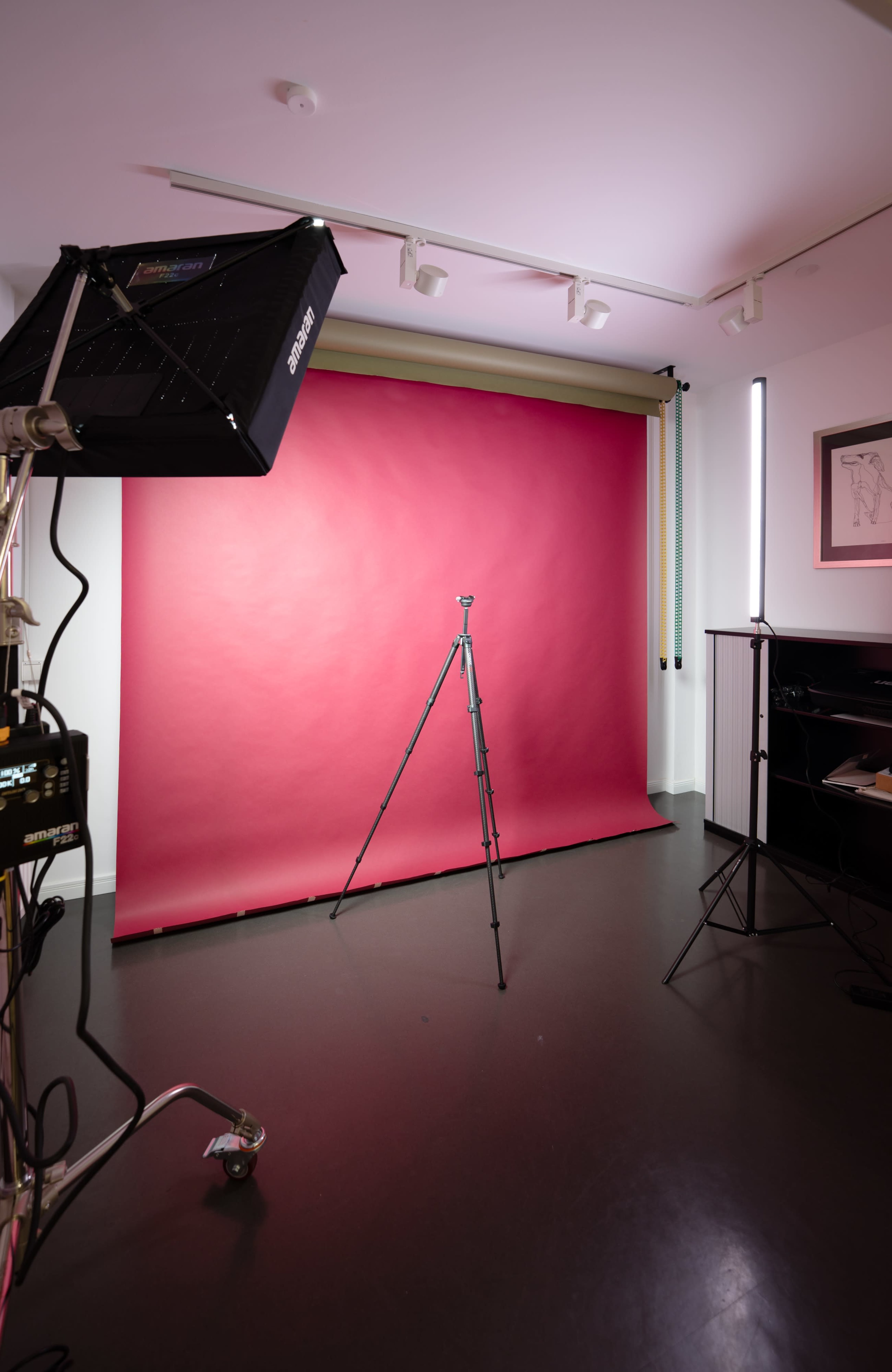 The image shows a photography studio setup featuring a red backdrop, a tripod, and studio lights positioned around the space.