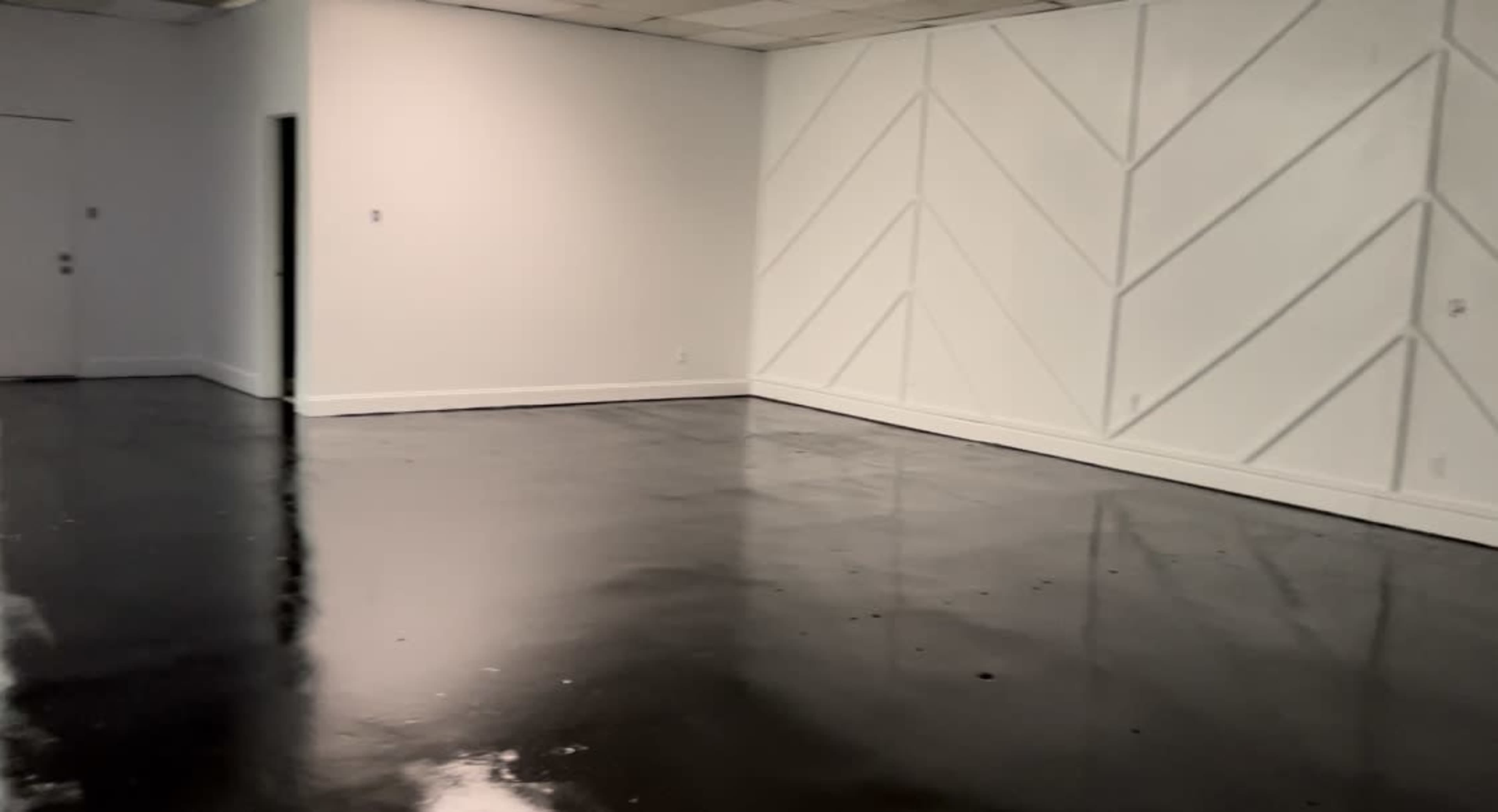 The image shows an empty room with glossy black flooring and a white wall featuring a geometric pattern.