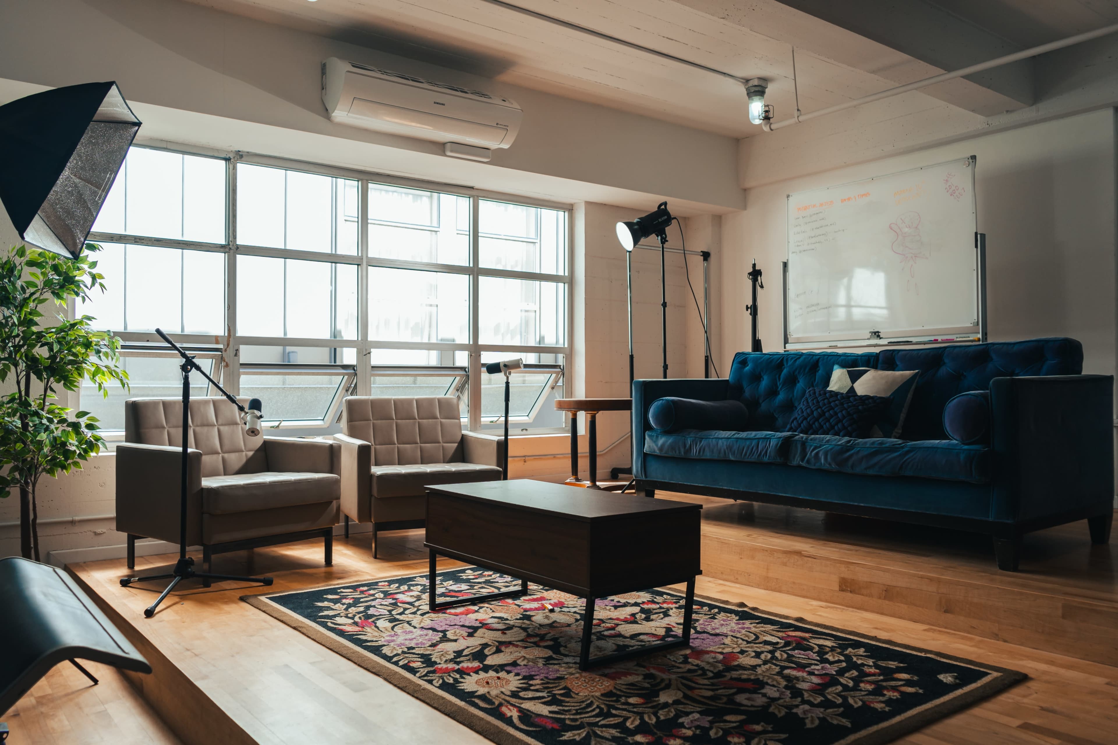 A modern living room with a blue sofa, two armchairs, a coffee table, and large windows allowing natural light.