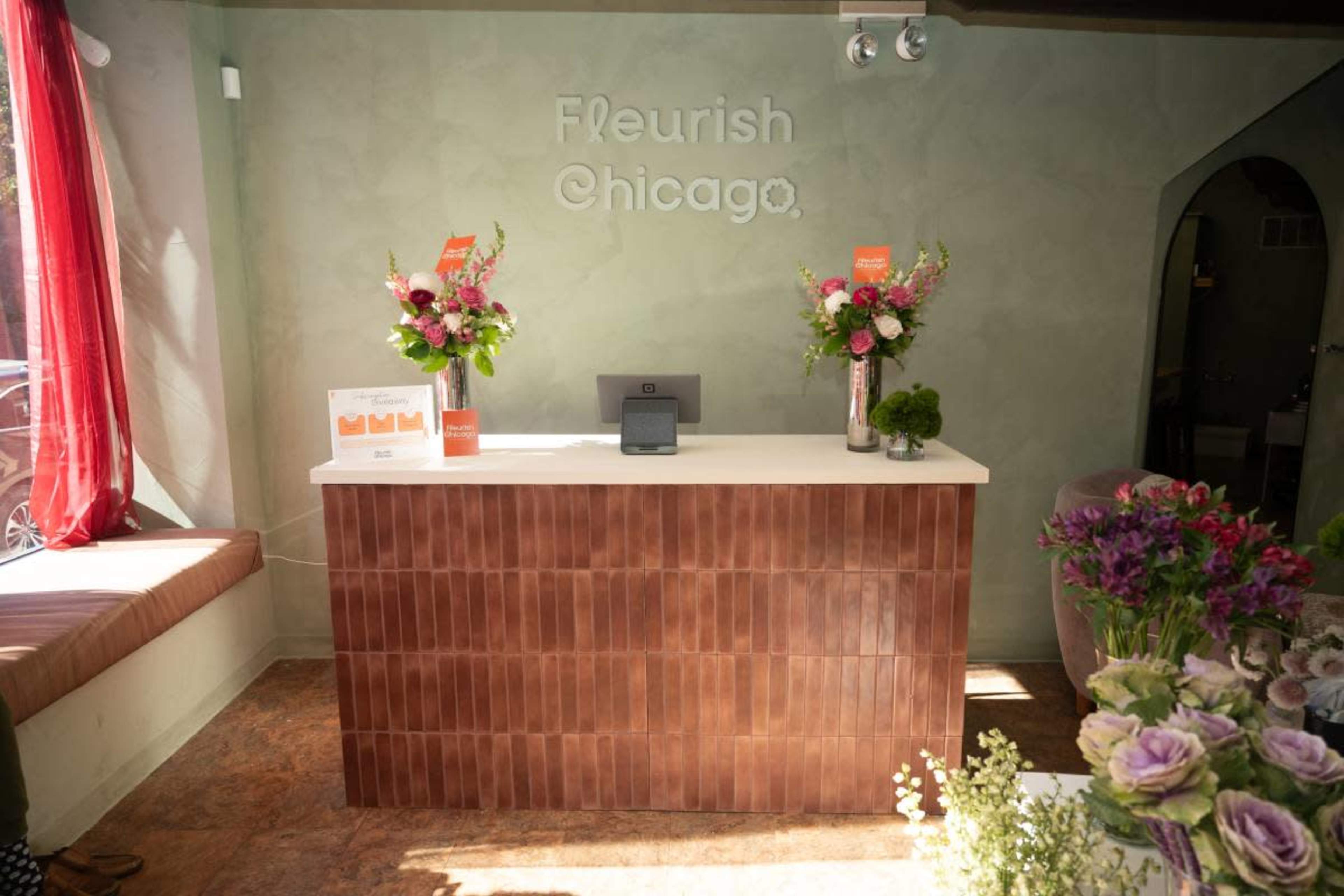 The image shows a reception area with a light green wall, a brown tiled counter, and floral arrangements on display.