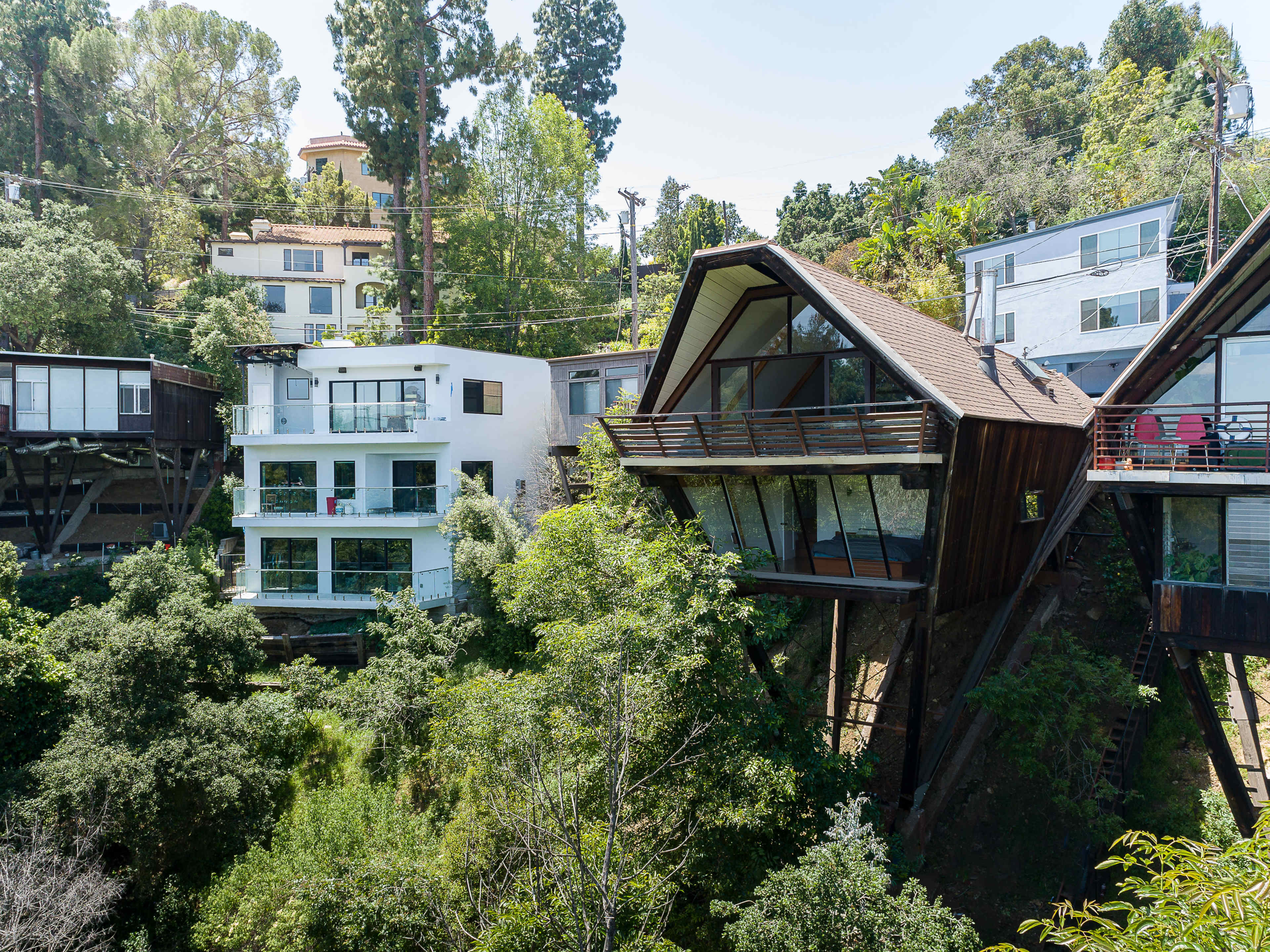 The image shows a collection of modern houses situated on a hillside, surrounded by dense greenery and trees.
