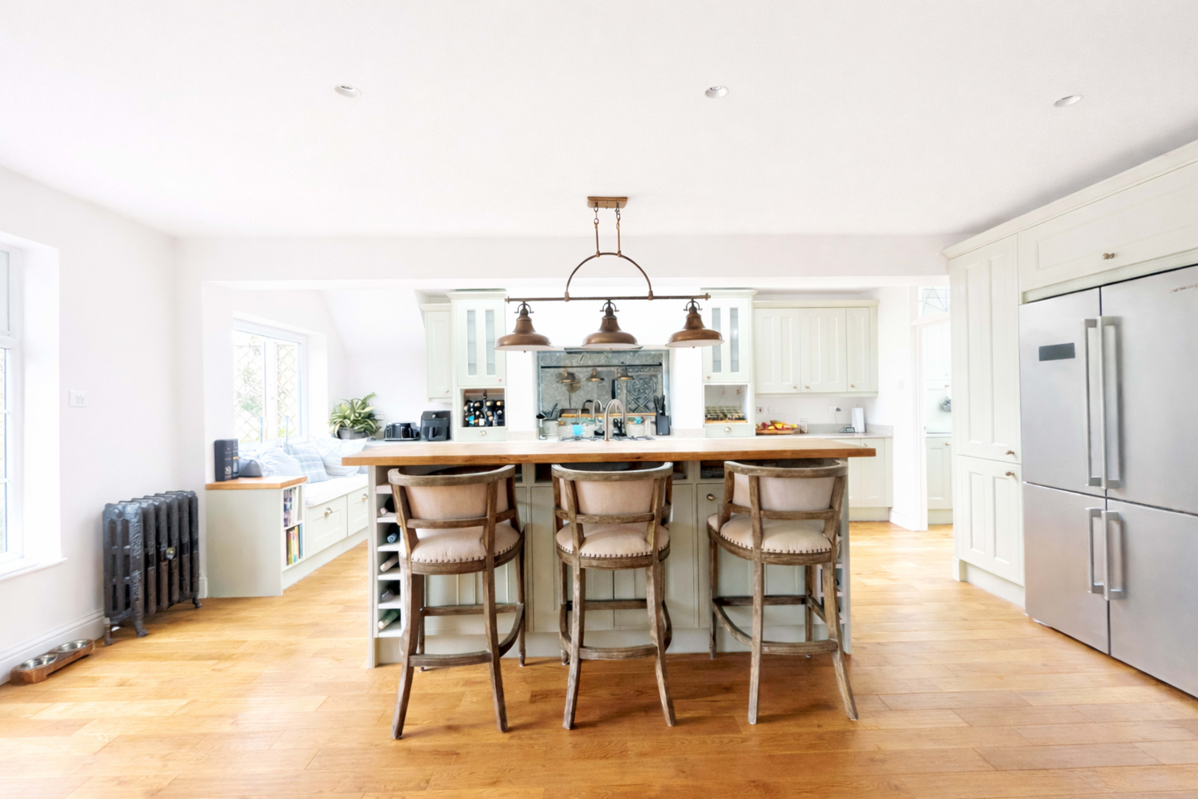 The image shows a modern kitchen featuring a central island with three stools, light-colored cabinetry, and stainless steel appliances.