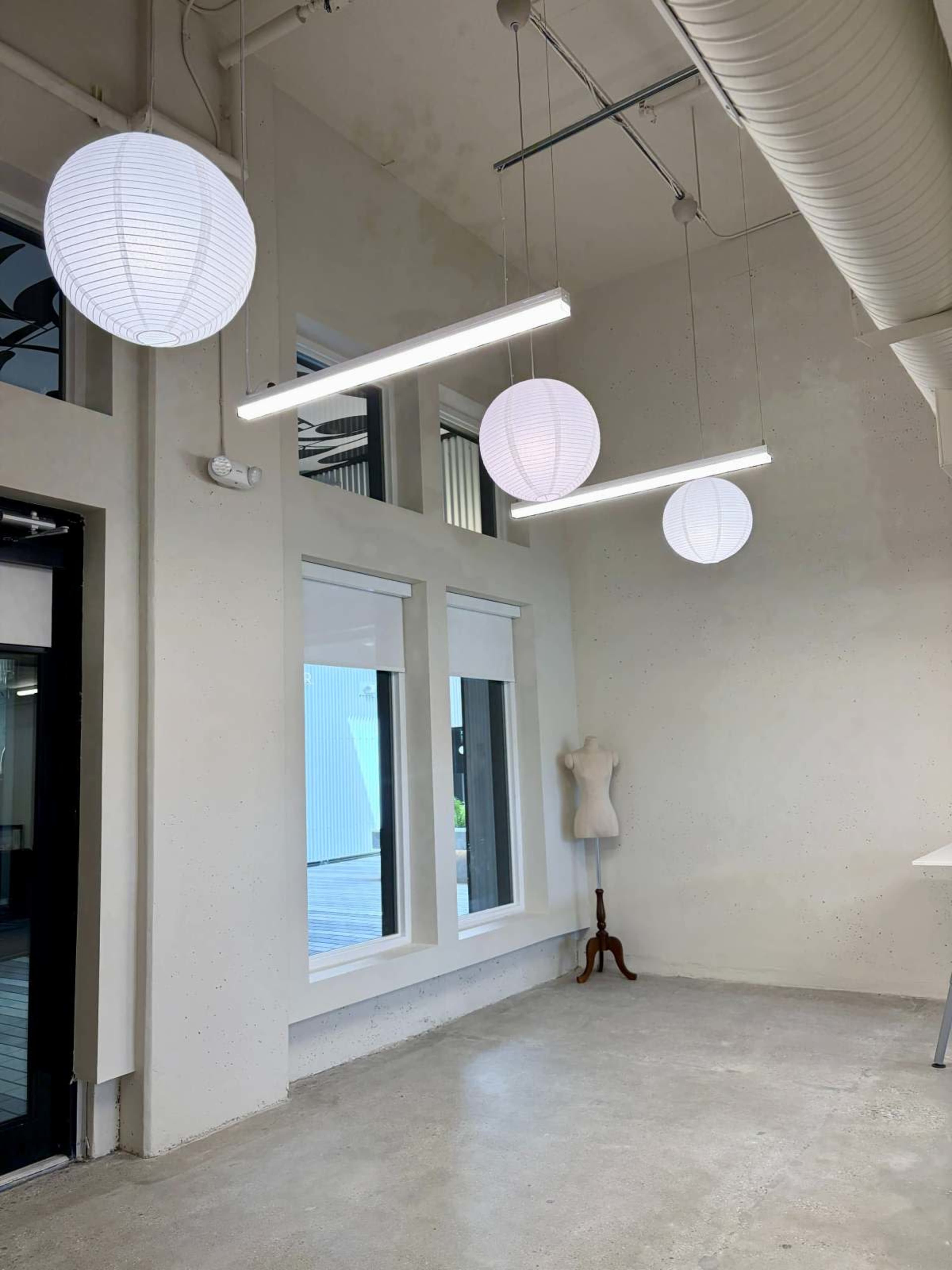 The image shows a modern interior space with three hanging light fixtures, a dress form on a stand, and large windows letting in natural light.