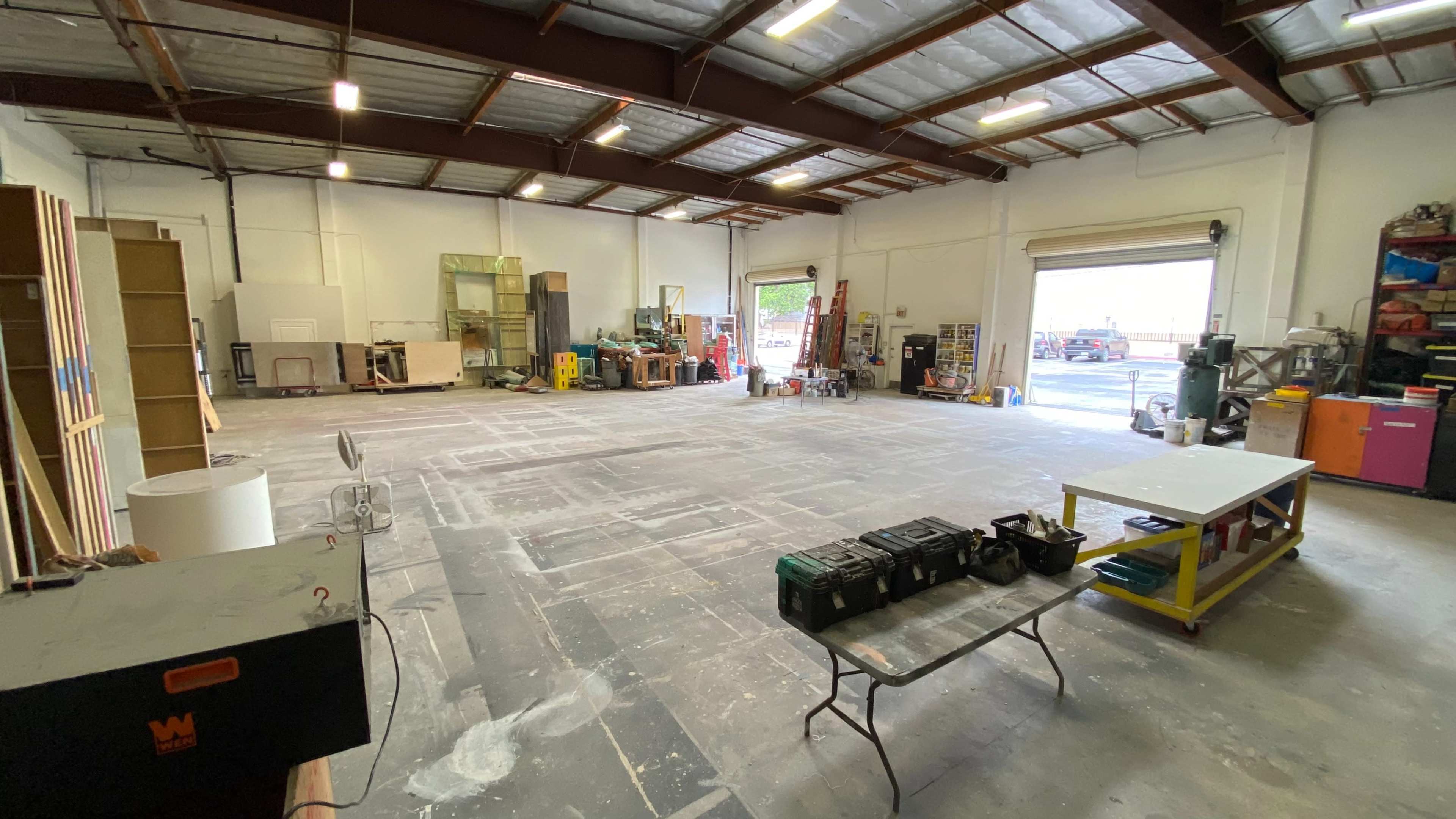 The image shows a spacious workshop or storage area with various equipment, tools, and a table in the foreground.