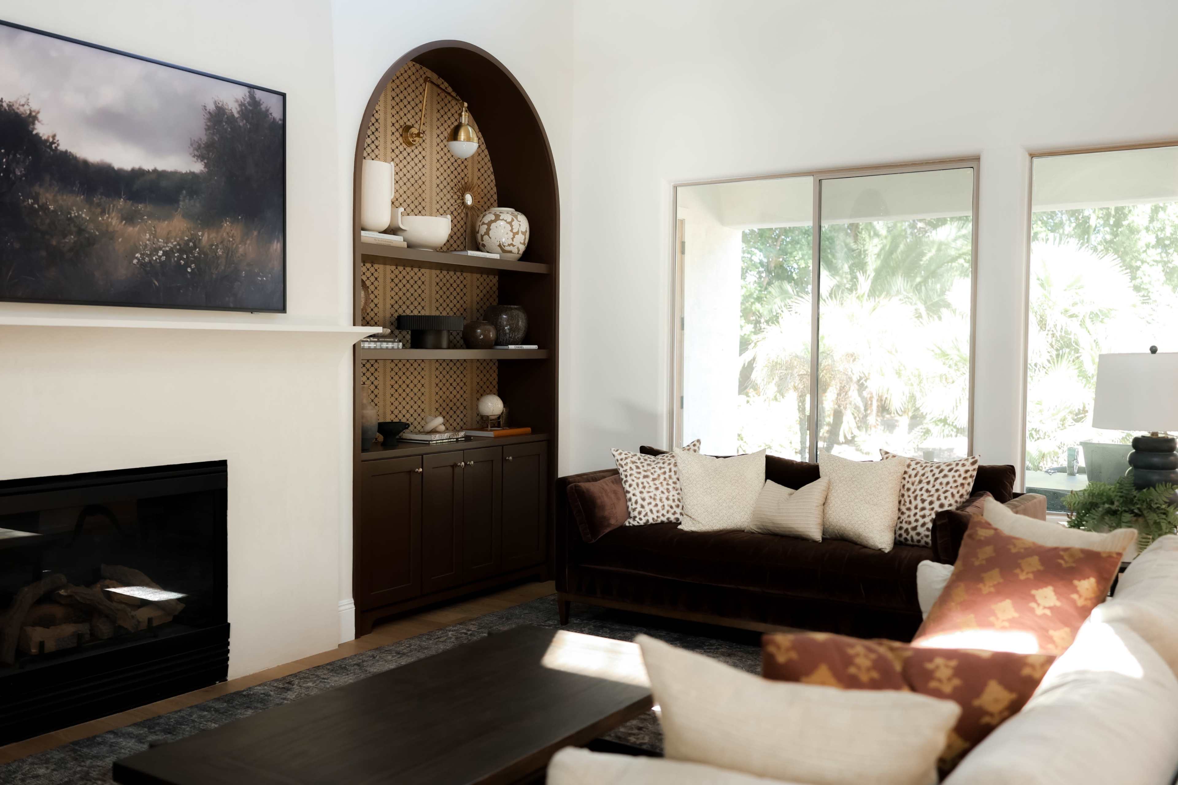 The image shows a bright living room featuring a dark sofa, a light-colored sectional, a coffee table, and various decorative items on a shelf against a wall.